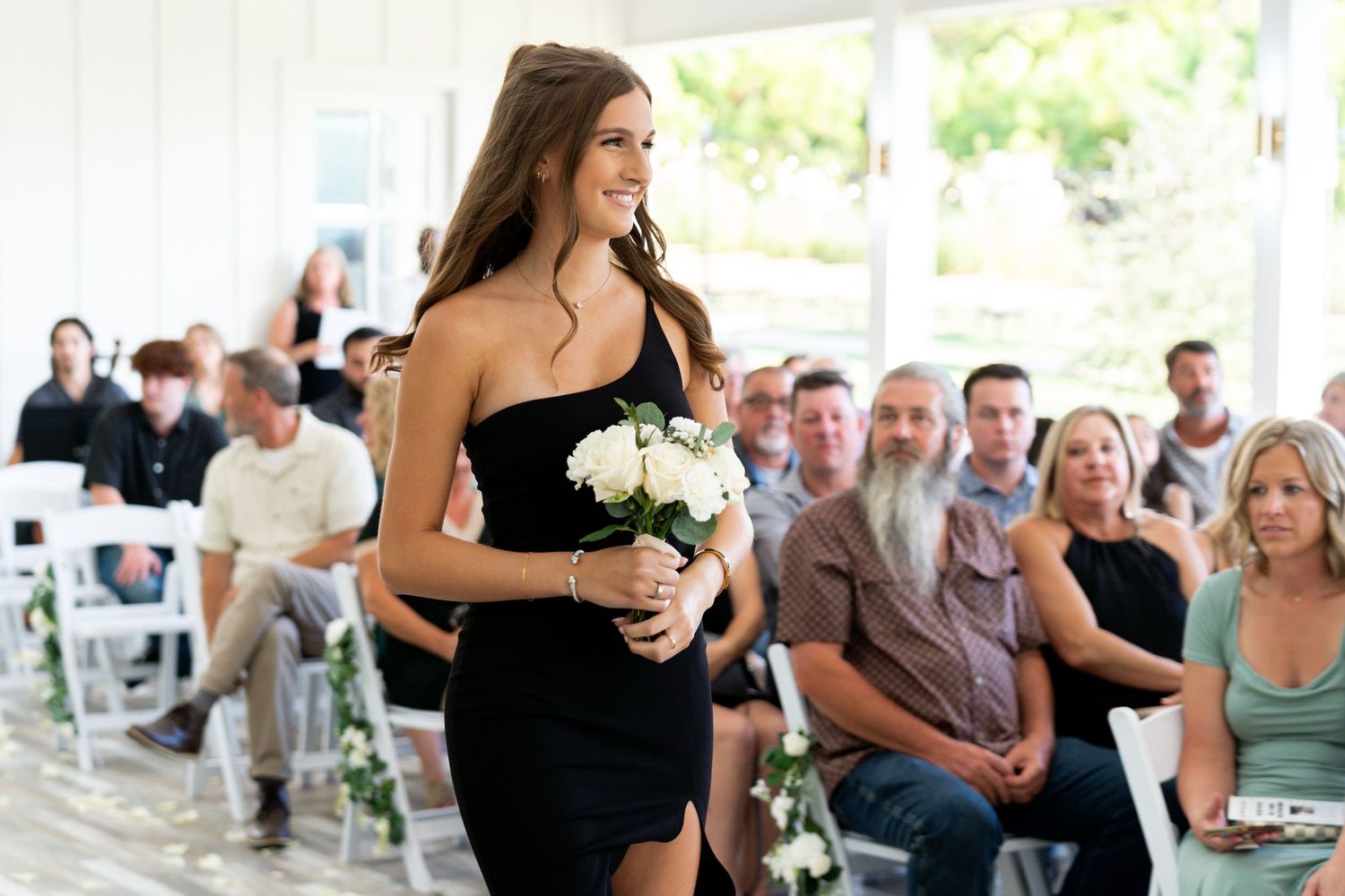 Wedding party members in black dresses dance and celebrate during an outdoor reception.