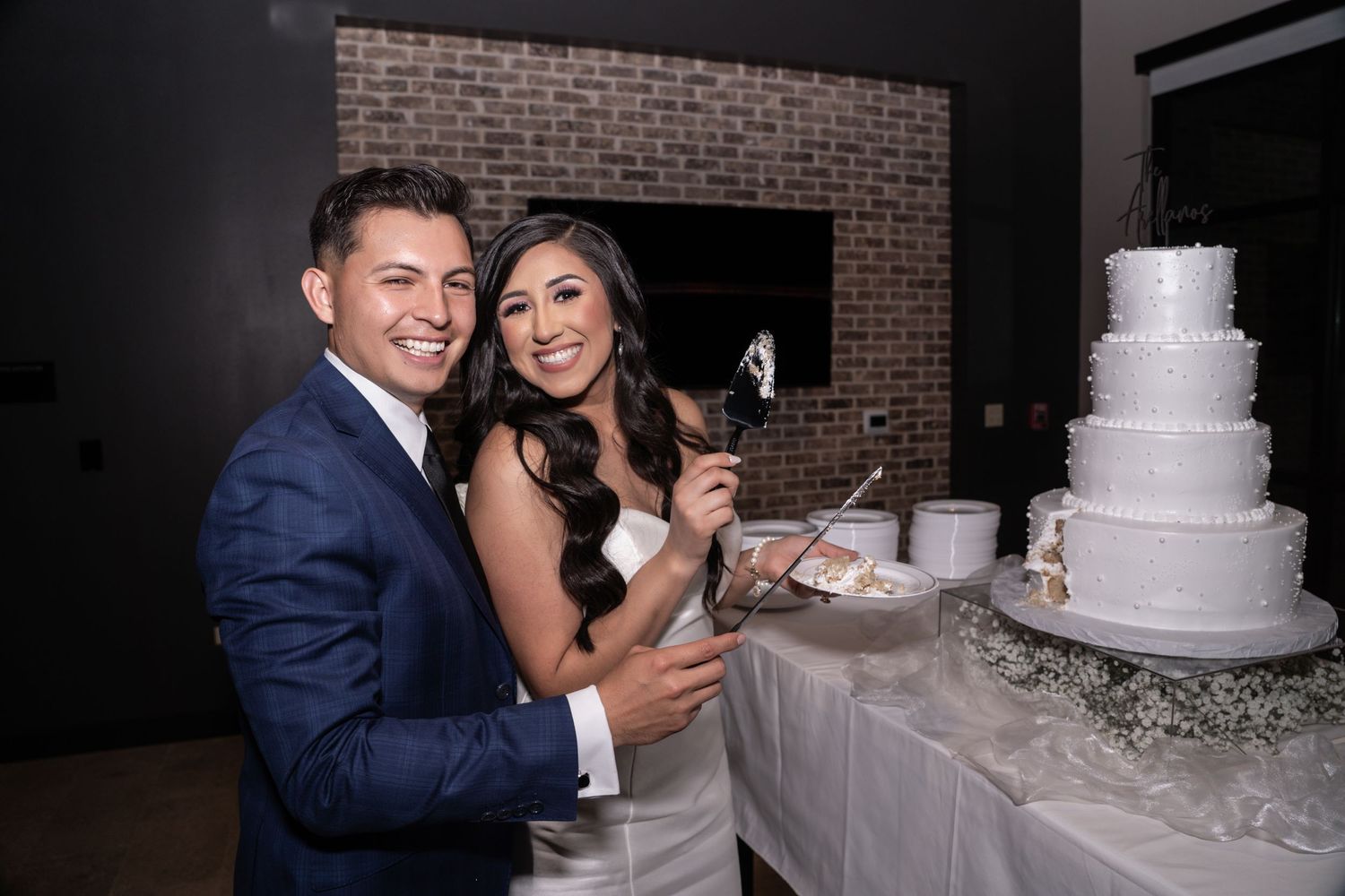 A wedding couple cuts their elegant white tiered cake together during their reception celebration.