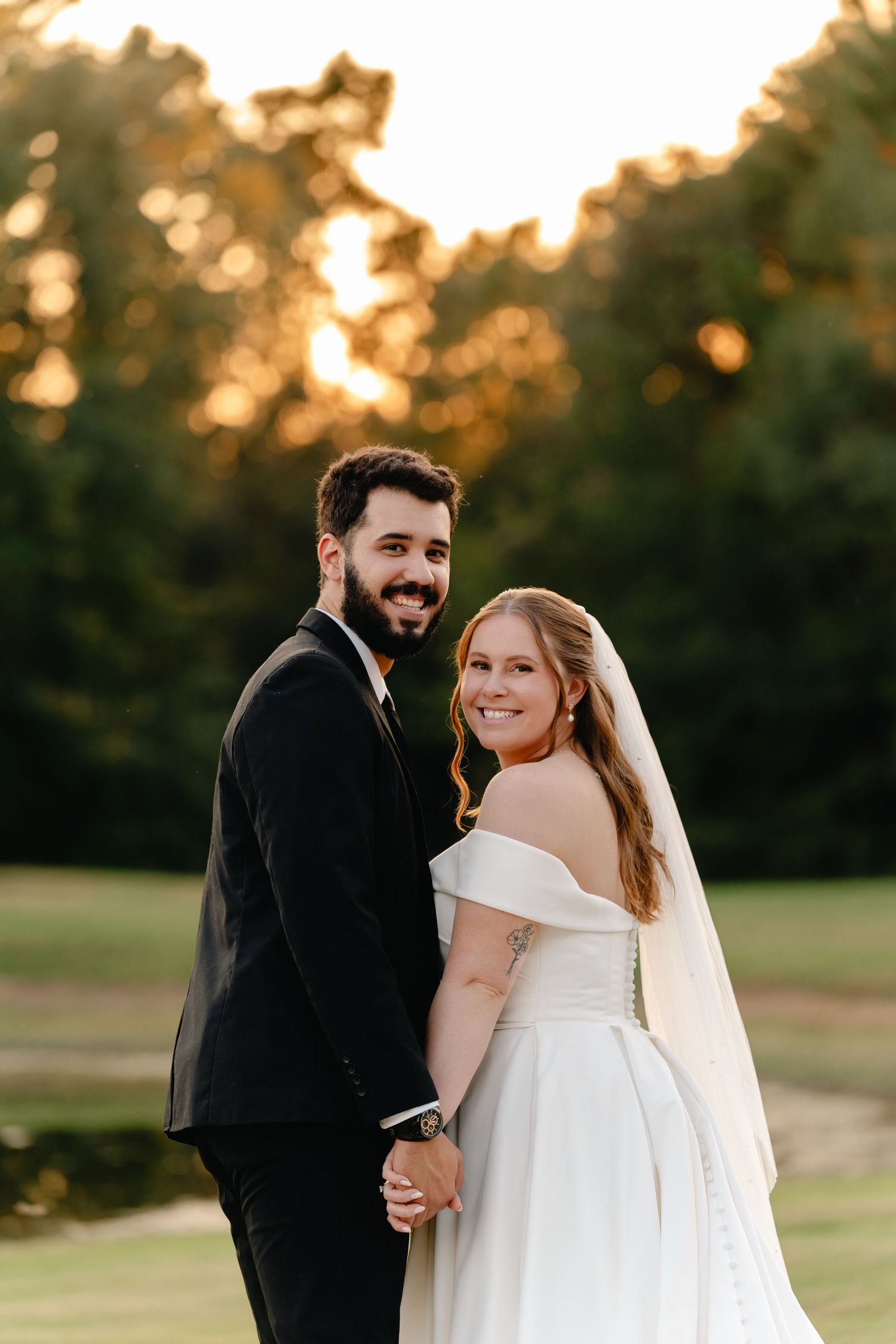Candid wedding portraits taken in a grassy field during sunset with warm golden lighting.