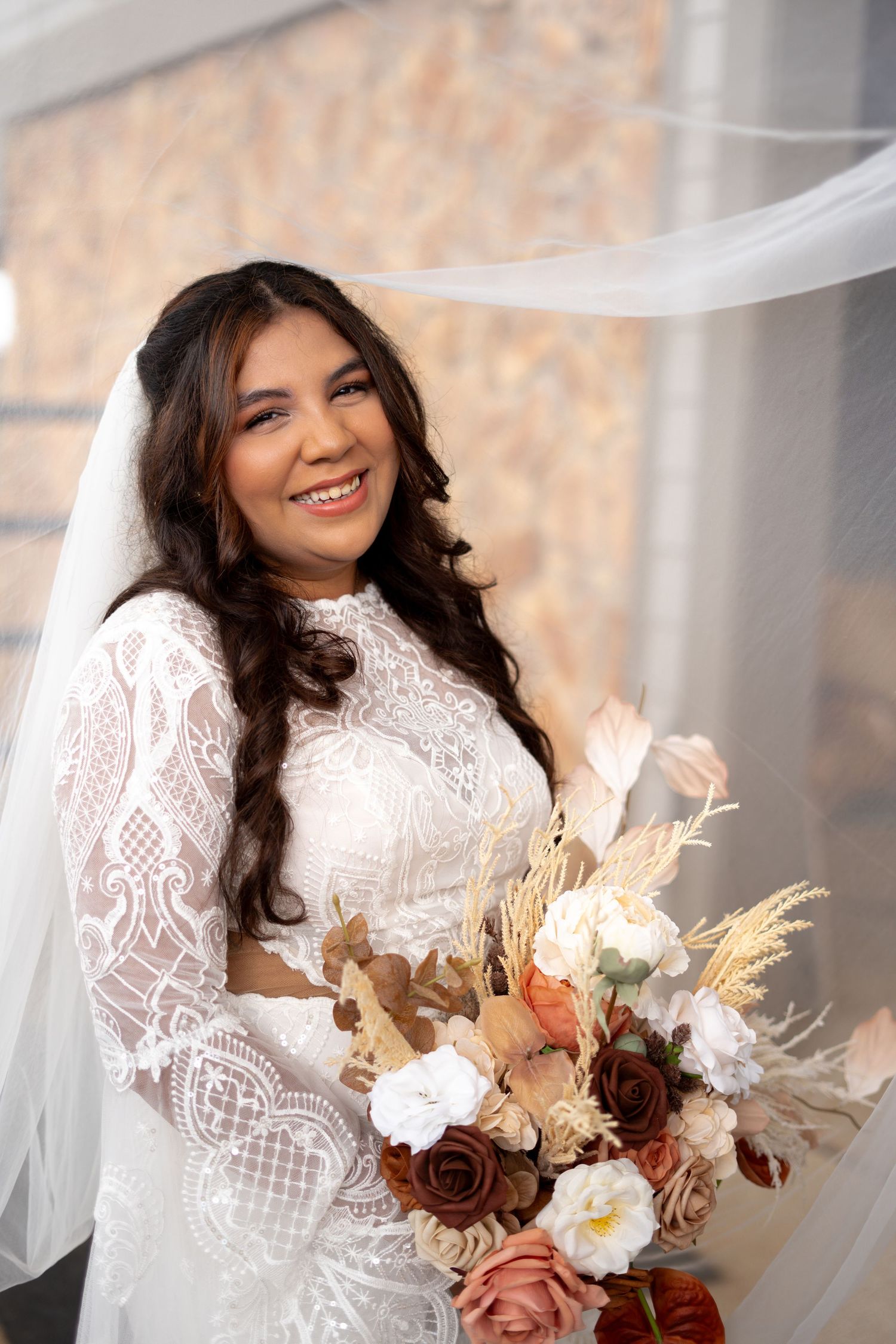 A bride in a lace wedding dress holds a bouquet with dried flowers and roses.