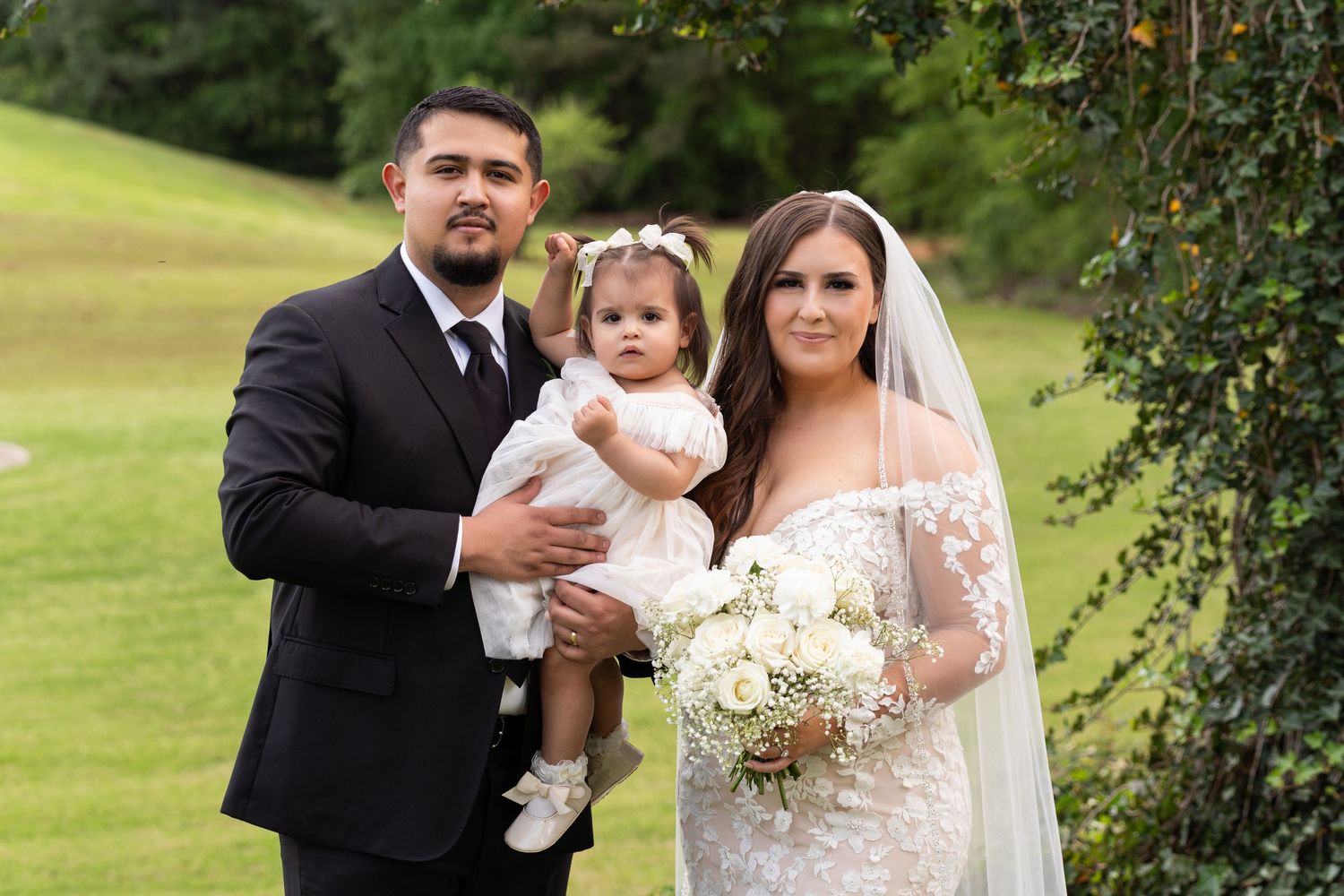 Wedding party poses on a lush green lawn with white floral bouquets during an outdoor celebration.
