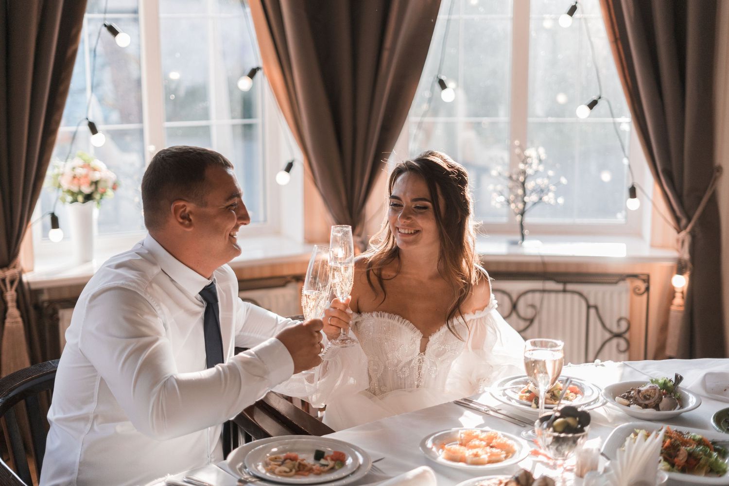 Couple enjoying dessert and sharing affectionate moments at an elegant dining table with window light.