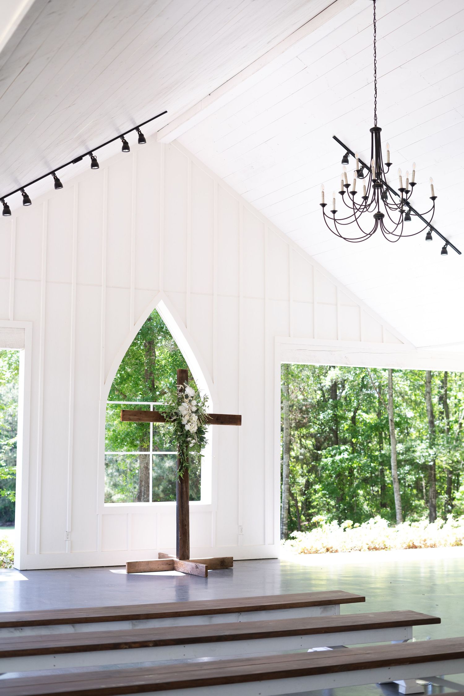 Interior view of a white chapel with tiered wooden seating and chandeliers showing multiple angles of the space.
