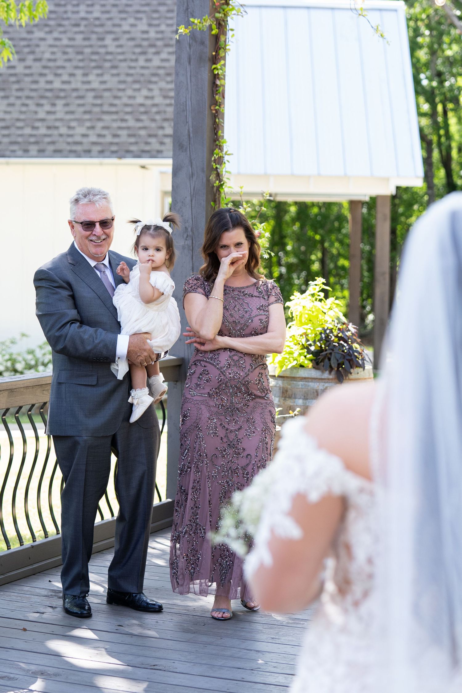 Emotional wedding moment captured on an outdoor deck with guests in formal attire watching the bride.