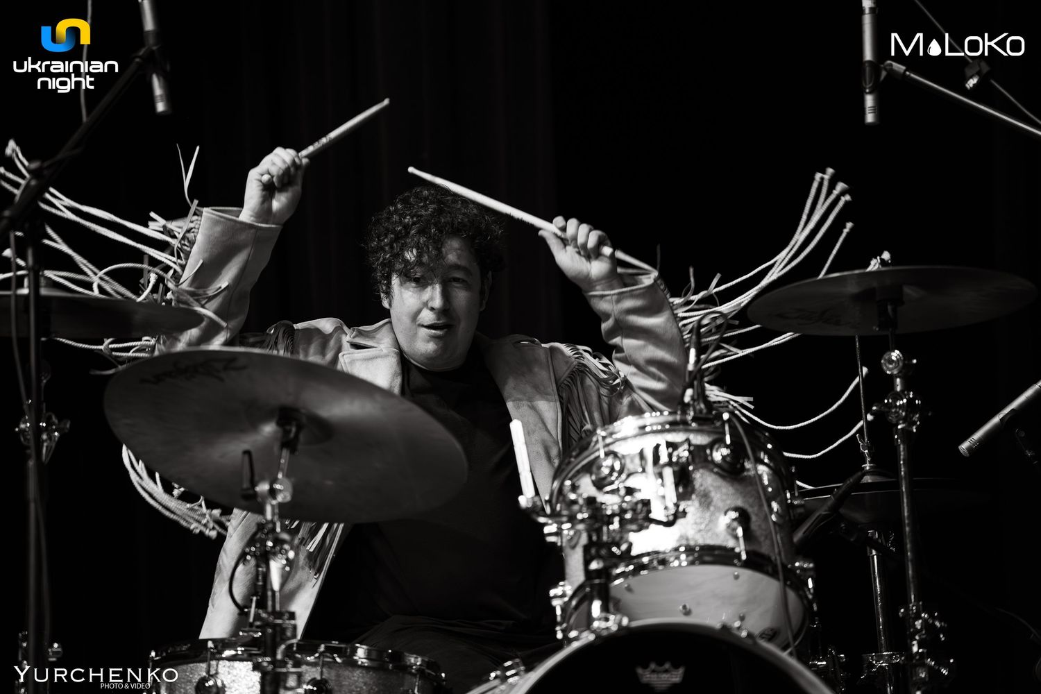 Drummer playing with intense energy on dark stage with dramatic lighting.