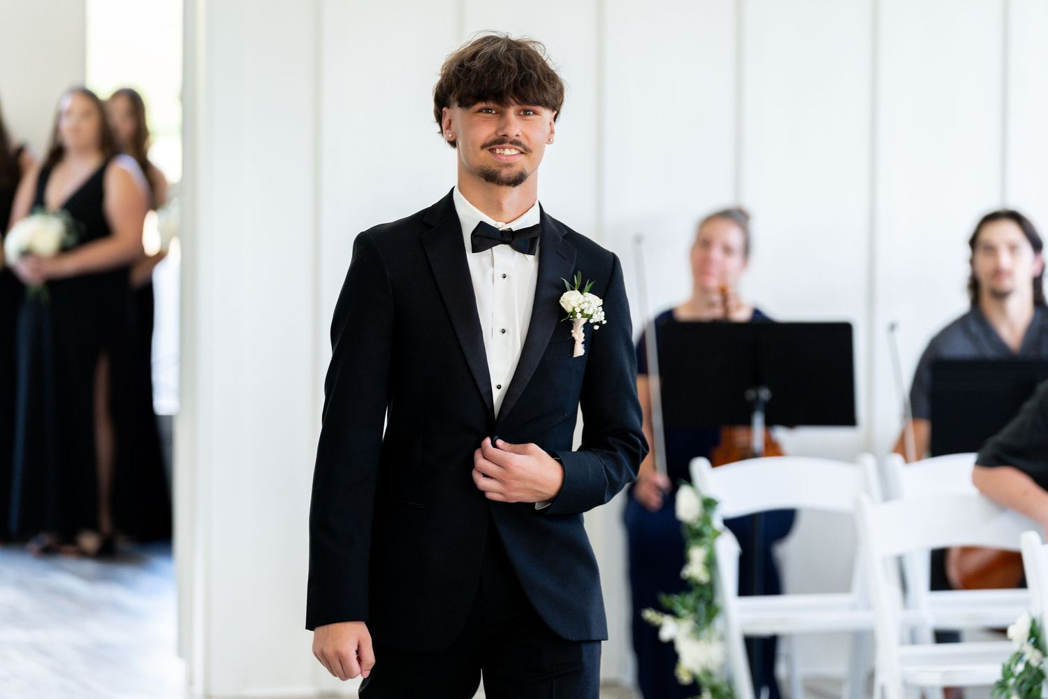 Wedding guests in formal attire celebrate and dance at an elegant reception with white decor and natural lighting.