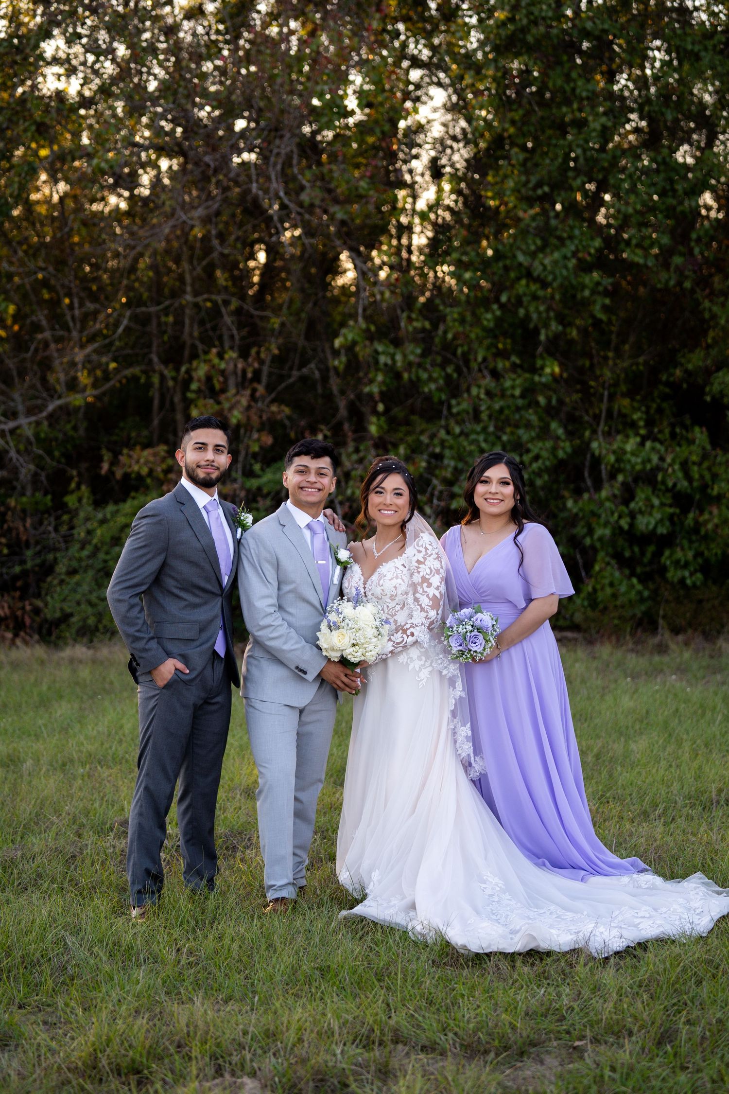 Wedding party members gather for outdoor portraits in purple dresses and gray suits.