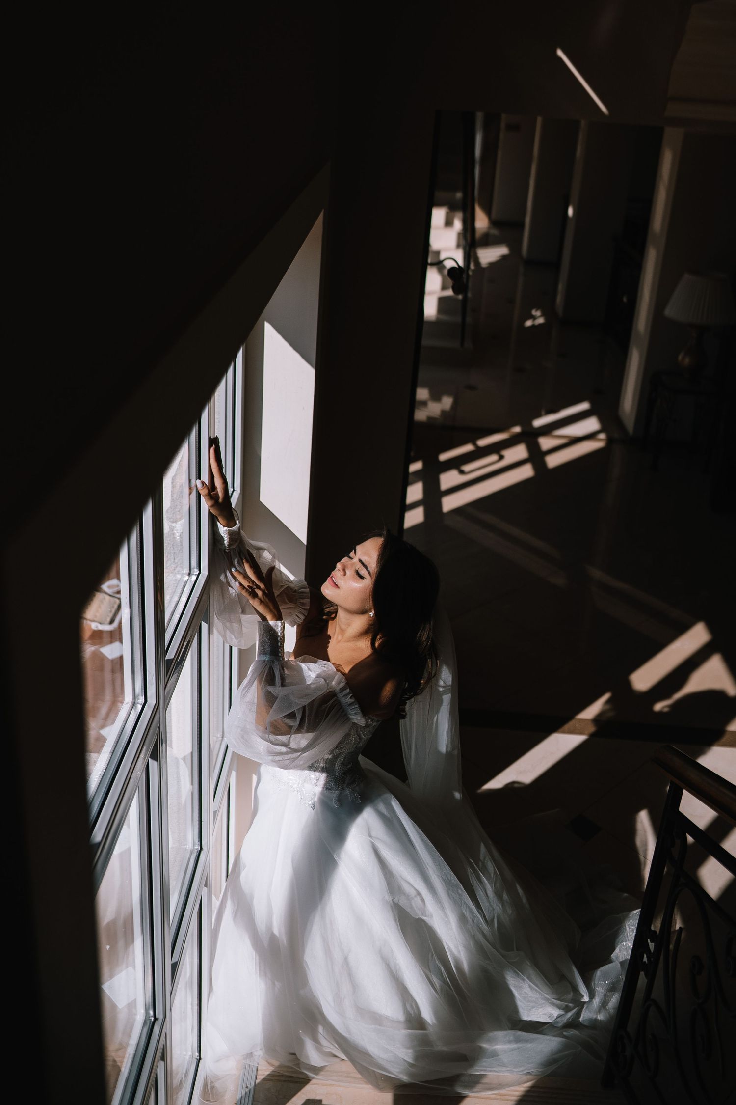A person in a flowing white wedding dress poses dramatically near large windows creating artistic silhouettes.