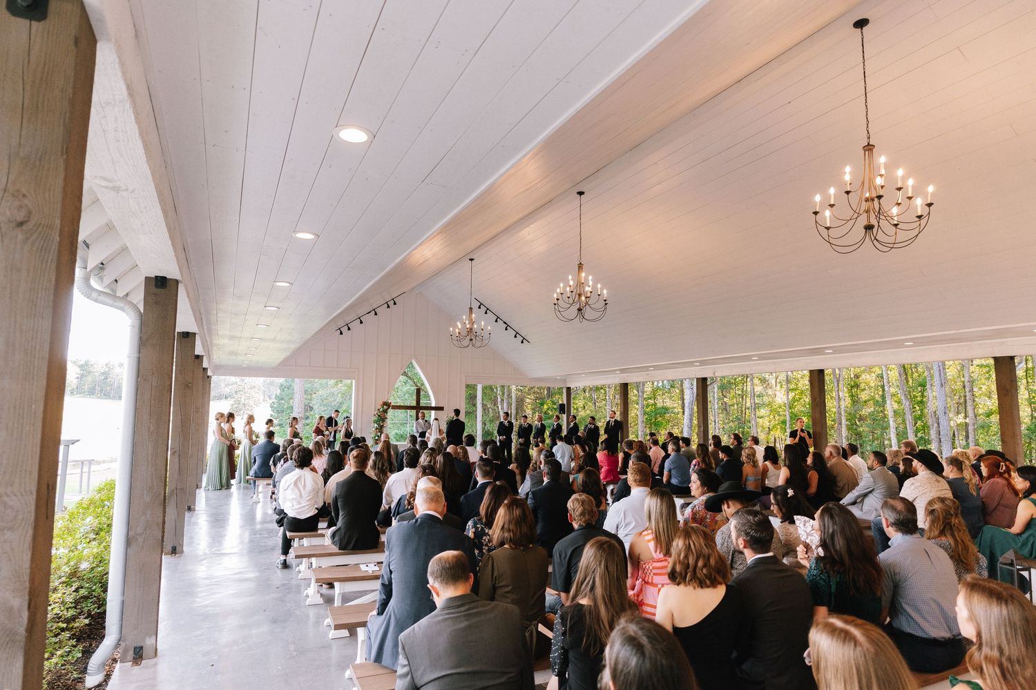 A wedding ceremony venue with white vaulted ceilings and crystal chandeliers filled with seated guests.