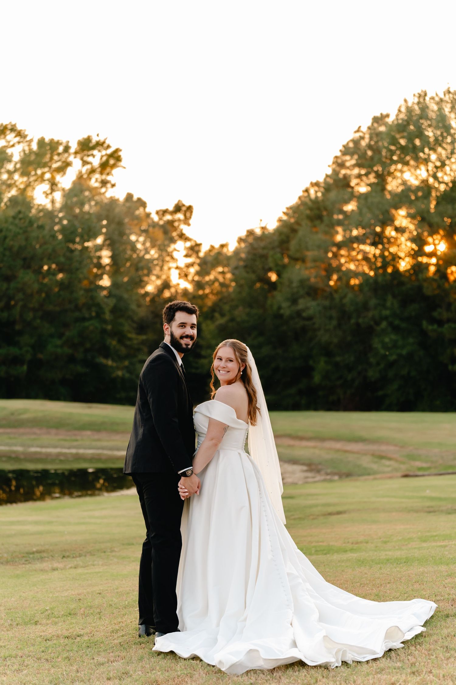 Newlyweds pose together on a rolling green field during golden hour with flowing white wedding dress.