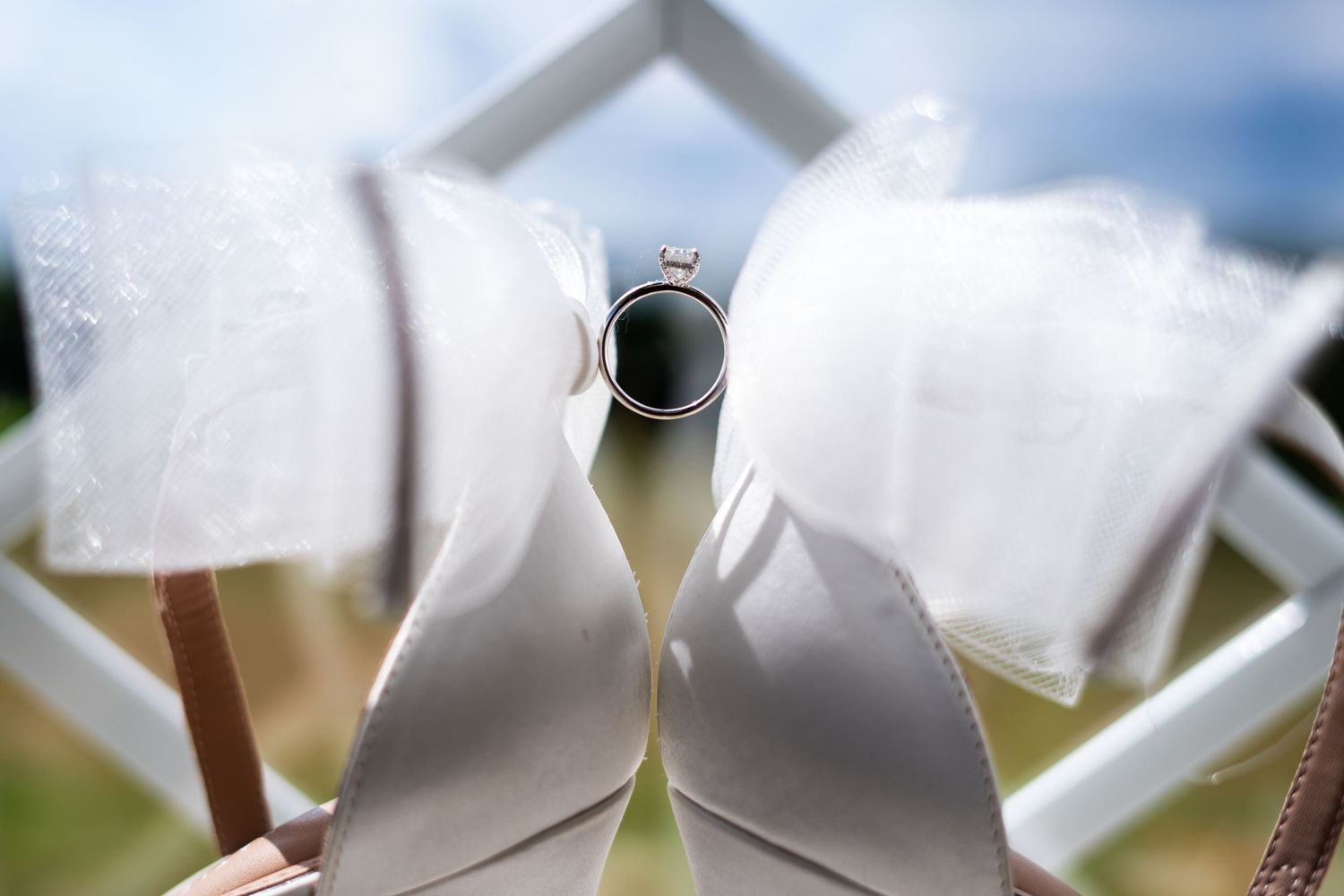 Close-up view of elegant white wedding shoes with decorative bow detail against a soft blurred background.