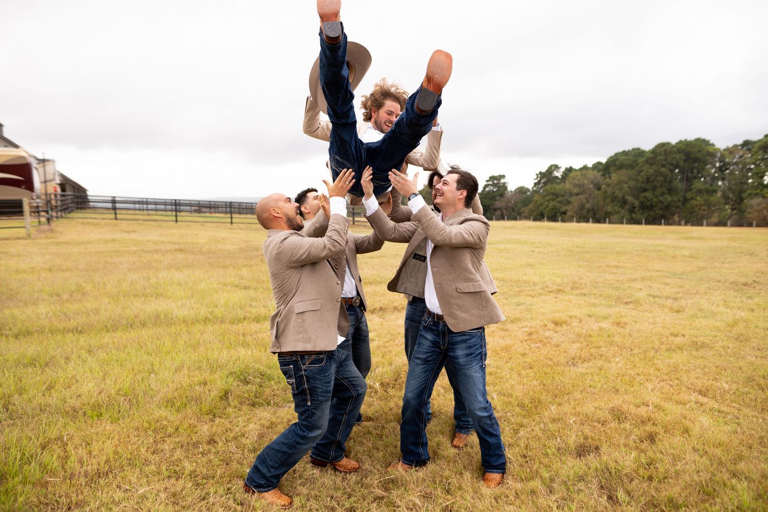 Wedding party having fun and jumping together in a sunny field with rolling hills.