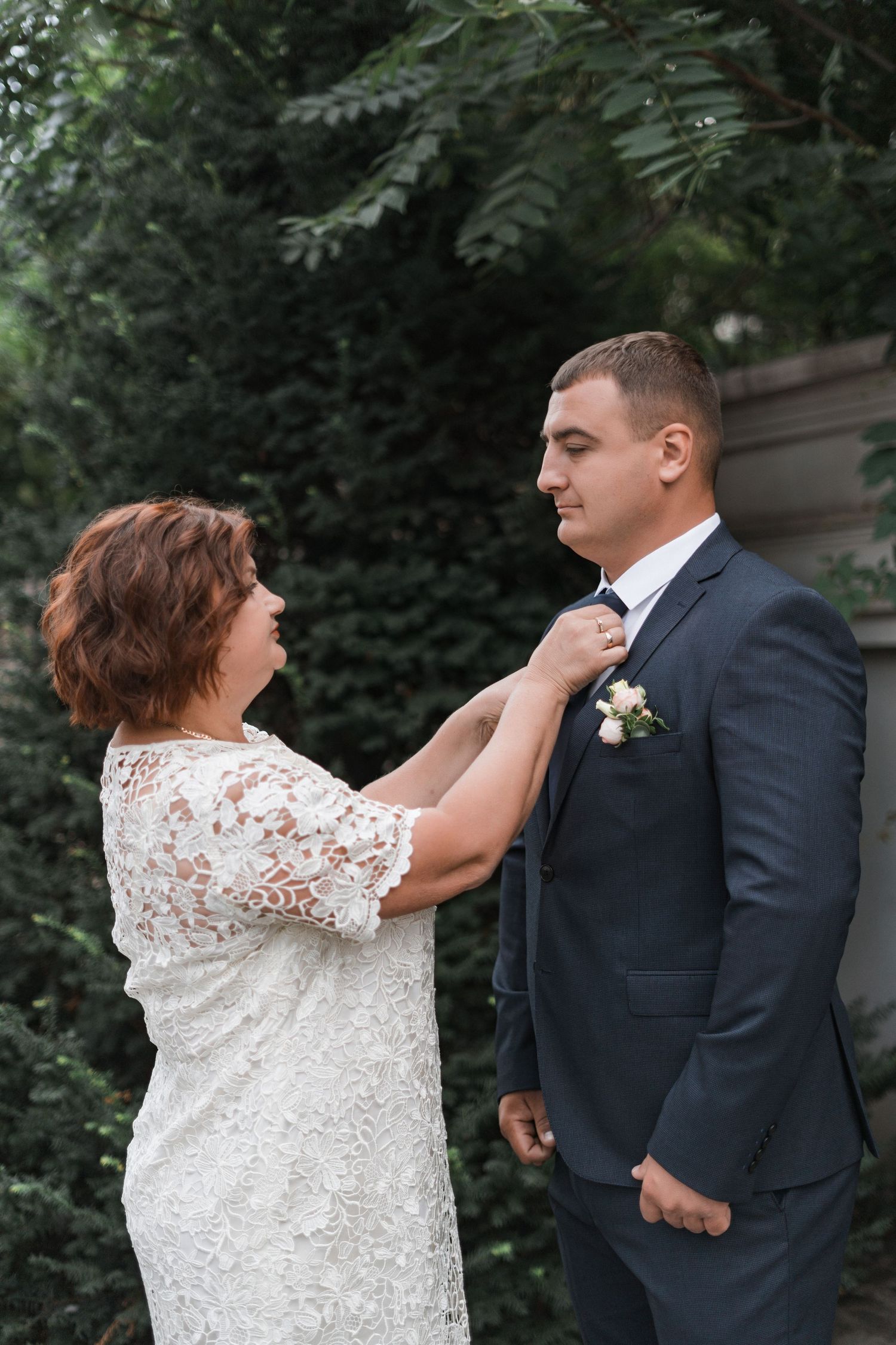 A sequence of wedding photos shows a bride in white lace adjusting the groom's boutonniere on his navy suit.