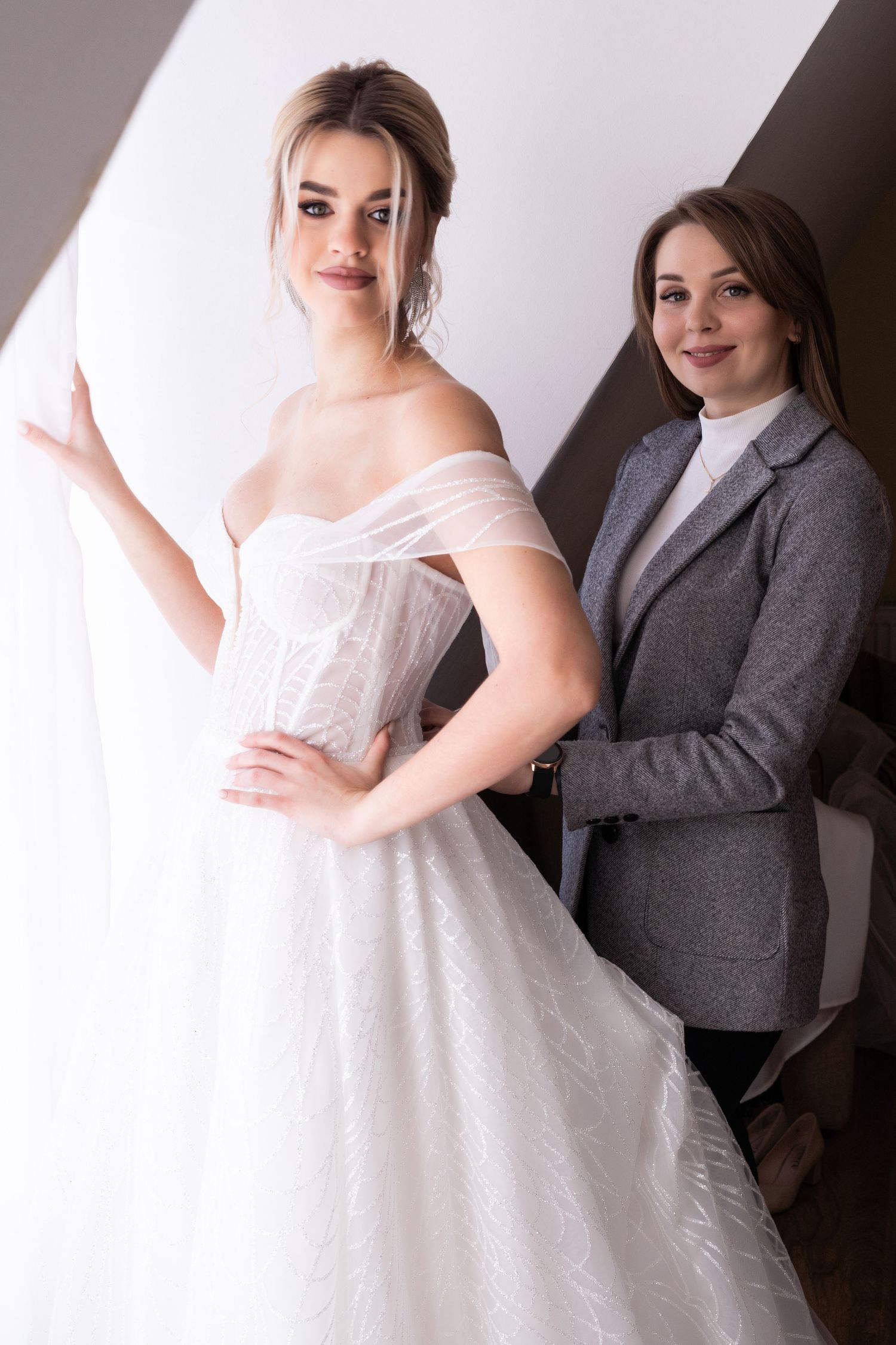 A bride in a white wedding dress poses with someone wearing a gray suit jacket against a dark background.