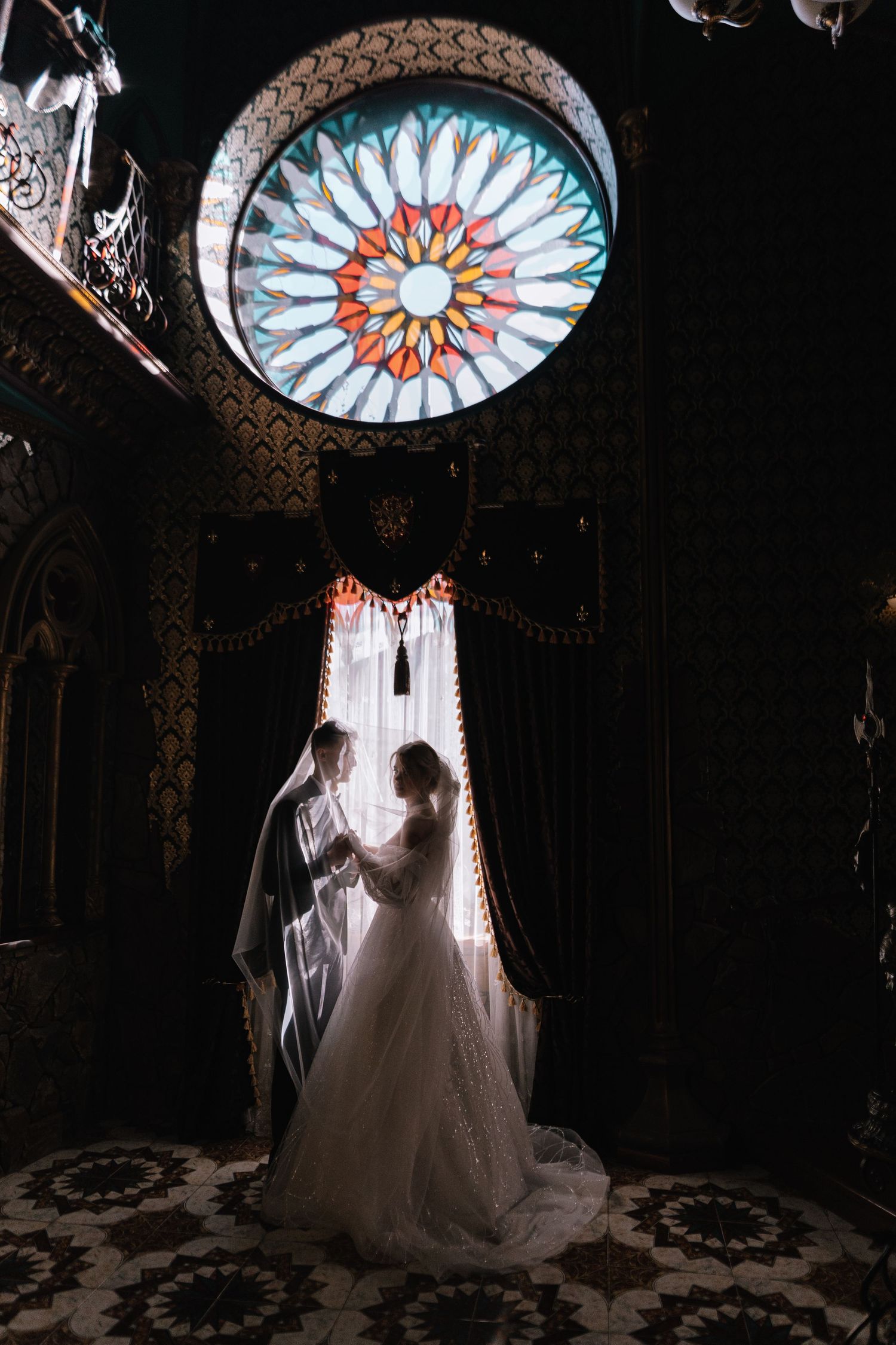 A silhouetted couple stands beneath an ornate stained glass rose window in a dramatic church interior.