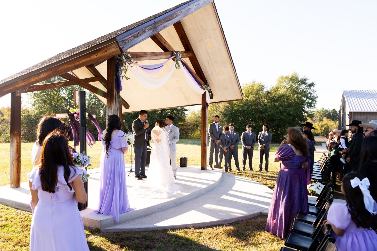 Wedding ceremony setup with purple decor and wooden beams against a natural outdoor backdrop.