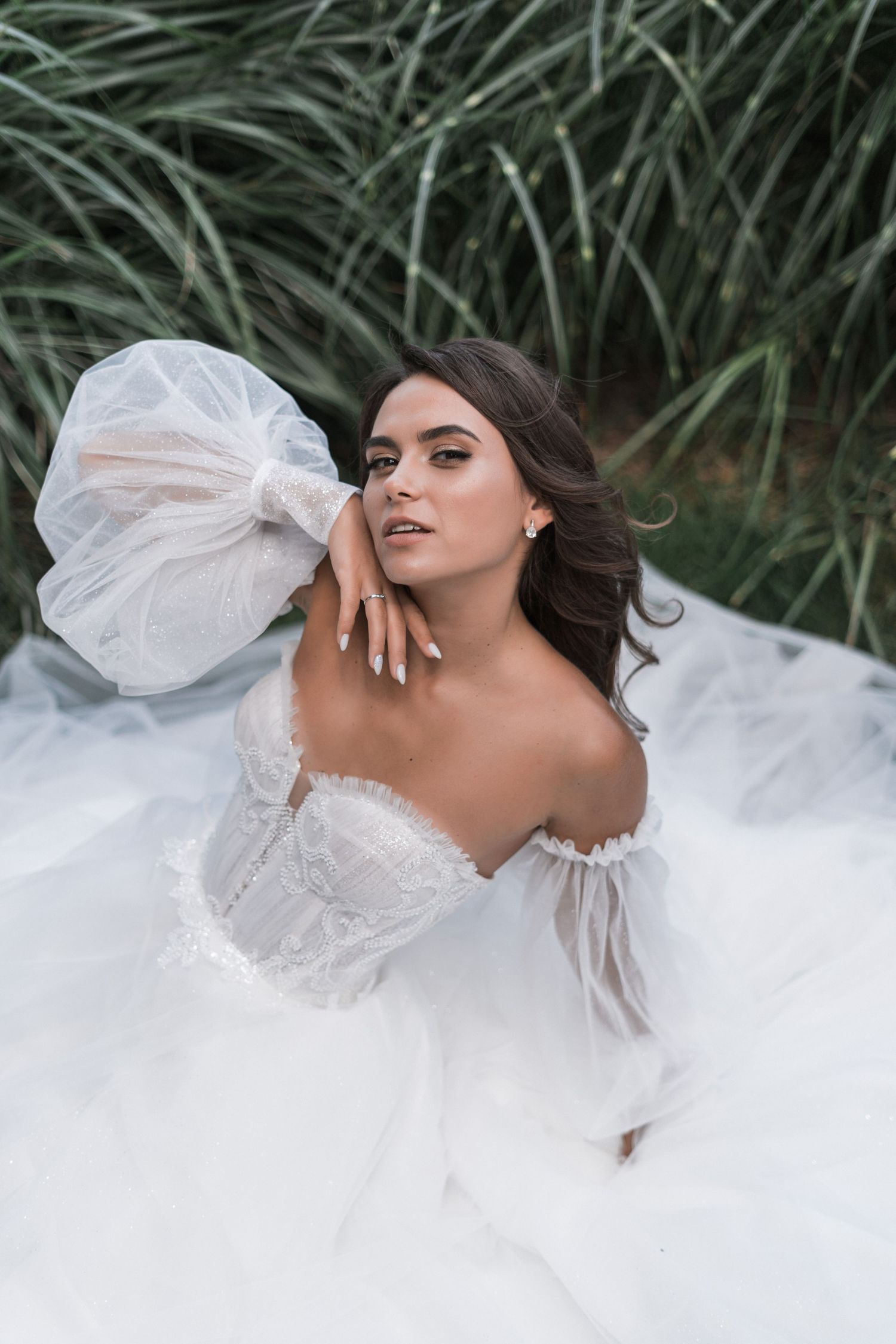 Ethereal bridal portrait featuring a flowing white wedding gown with puffy sleeves against a backdrop of green palm fronds.