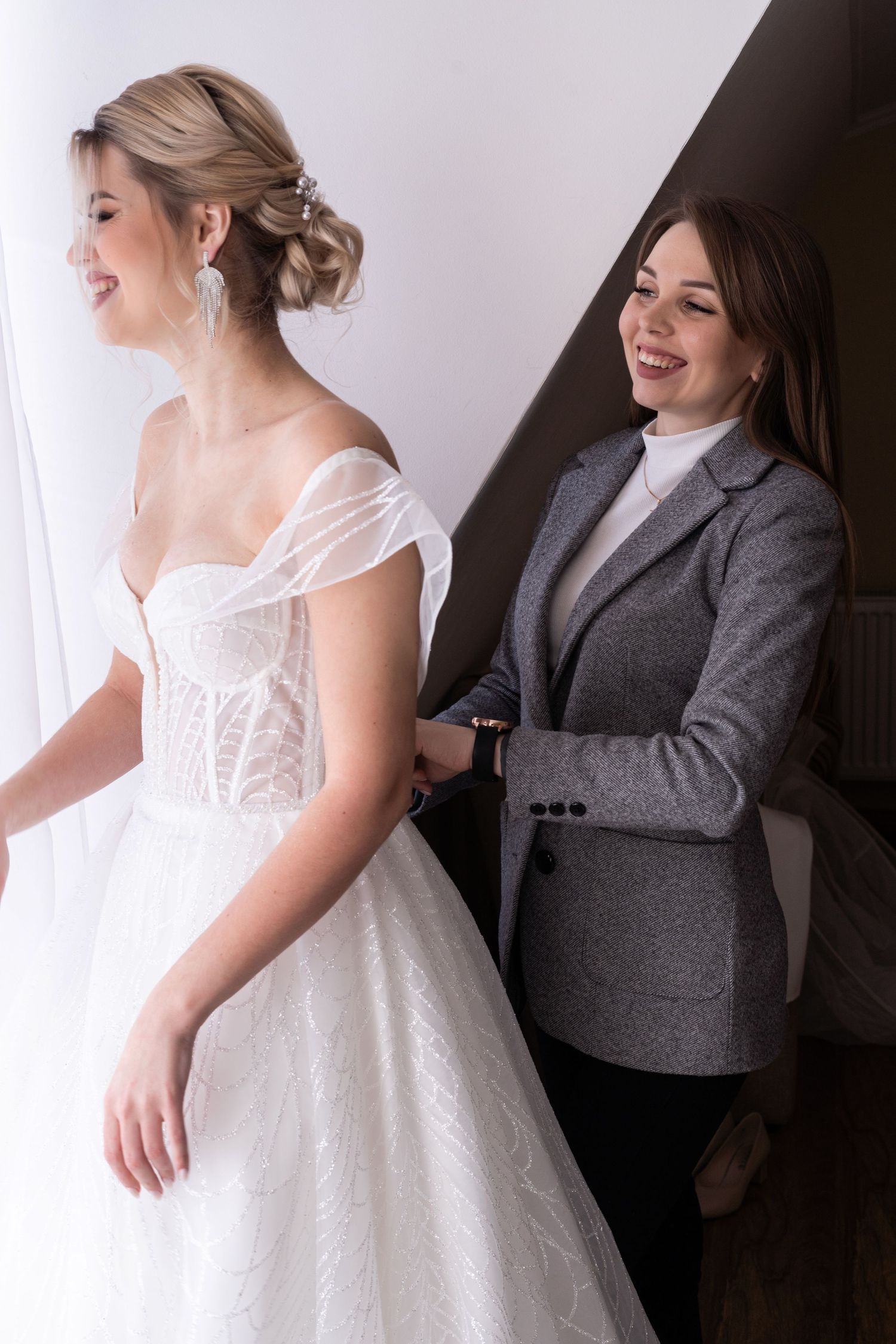 A joyful moment captured as someone helps adjust a flowing white wedding dress in a getting ready scene.