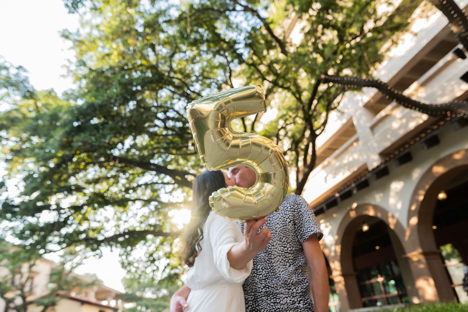 Couple embraces under string lights and trees during an outdoor photo session.