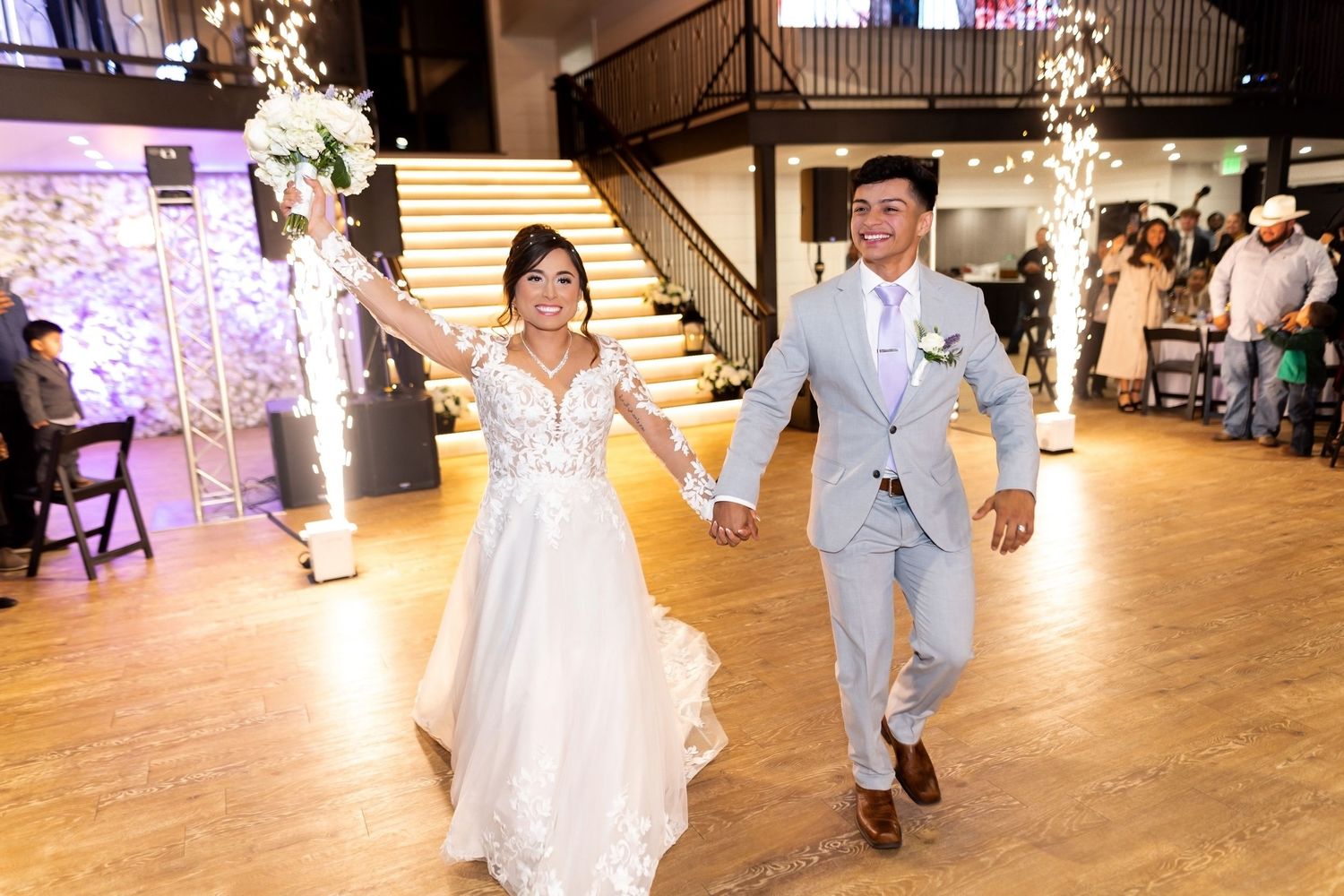 Wedding couple dances and celebrates in reception venue with sparkler effects and wooden floors.