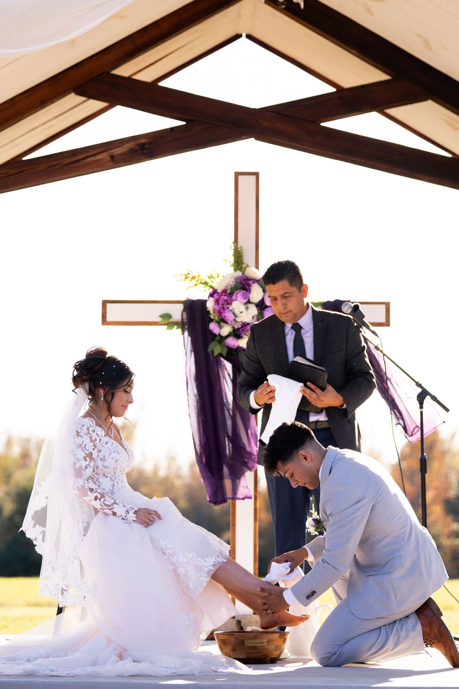 Traditional foot washing ceremony during wedding with cross and purple floral decorations.