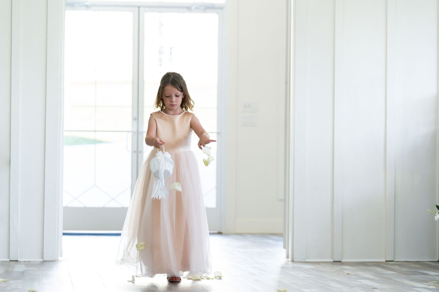 A child in a flowing pink dress twirls gracefully in a bright white studio setting.