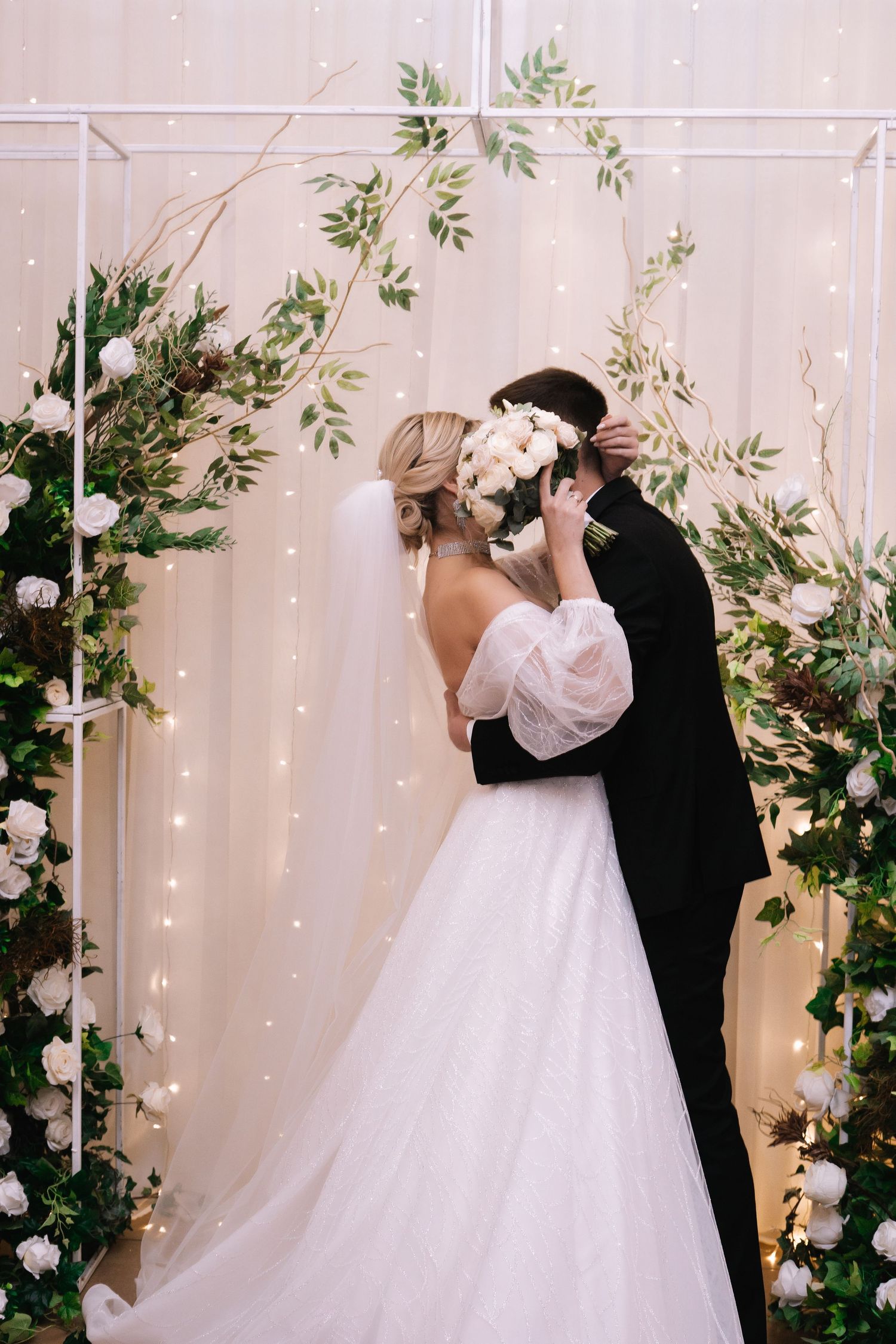 A wedding couple shares their first dance surrounded by twinkling lights and greenery decorations at their reception.