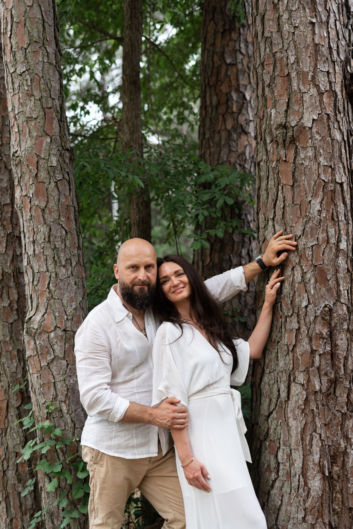 Romantic couple photoshoot in a pine forest wearing coordinated white outfits.