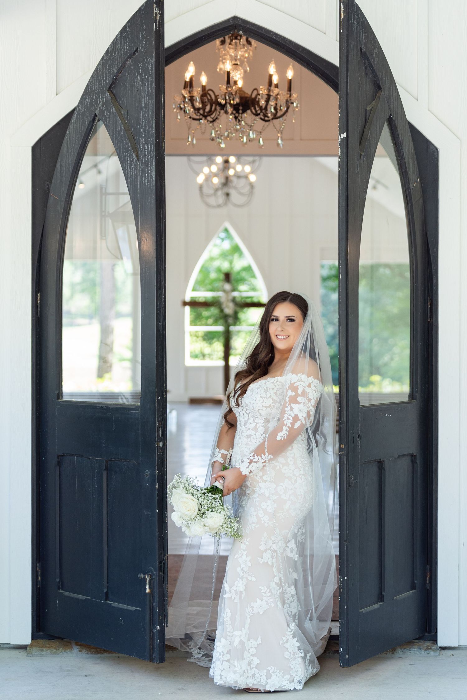 Elegant wedding venue interior features black French doors, white walls, and crystal chandeliers in a classic setting.