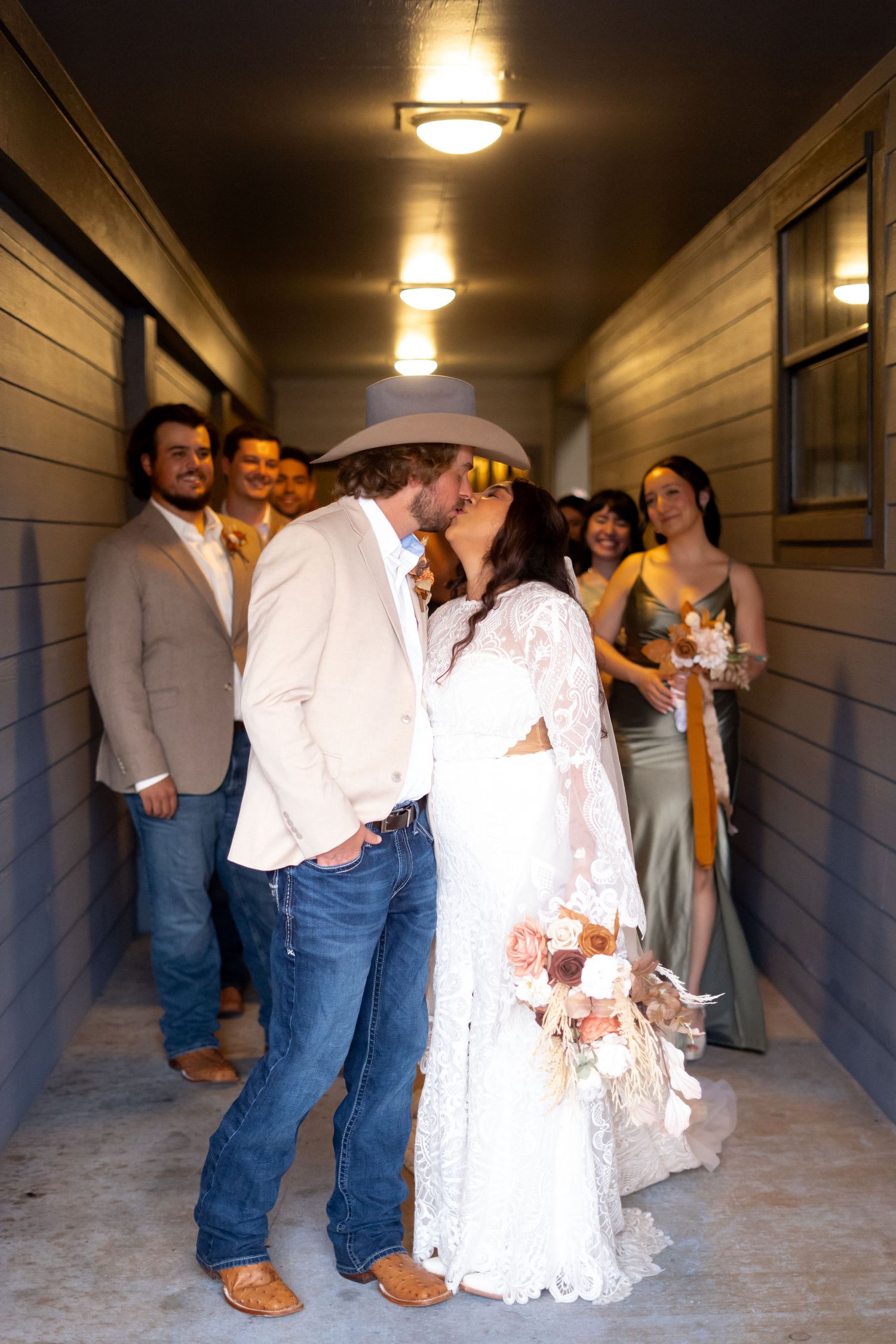 Wedding party celebrating in a dimly lit hallway with rustic wooden walls.