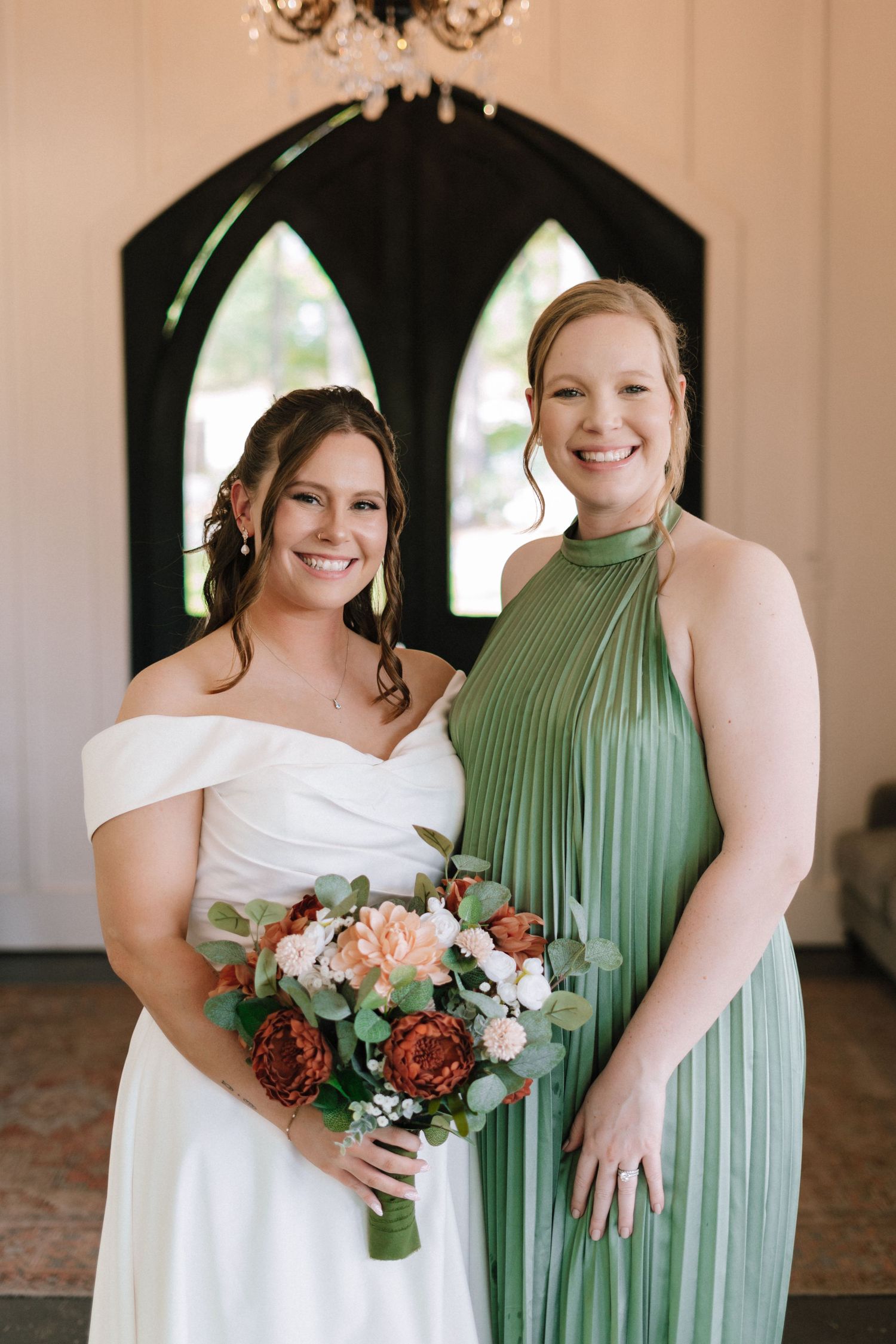 Wedding party members in sage green bridesmaid dress and white bridal gown pose with floral bouquets.