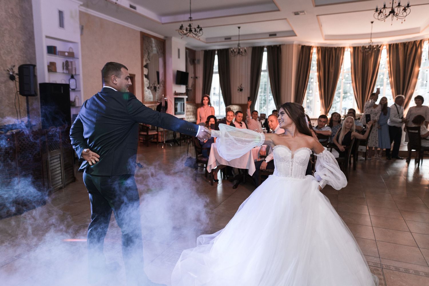 Wedding couple dances in a grand ballroom filled with fog effects and romantic lighting during their first dance.