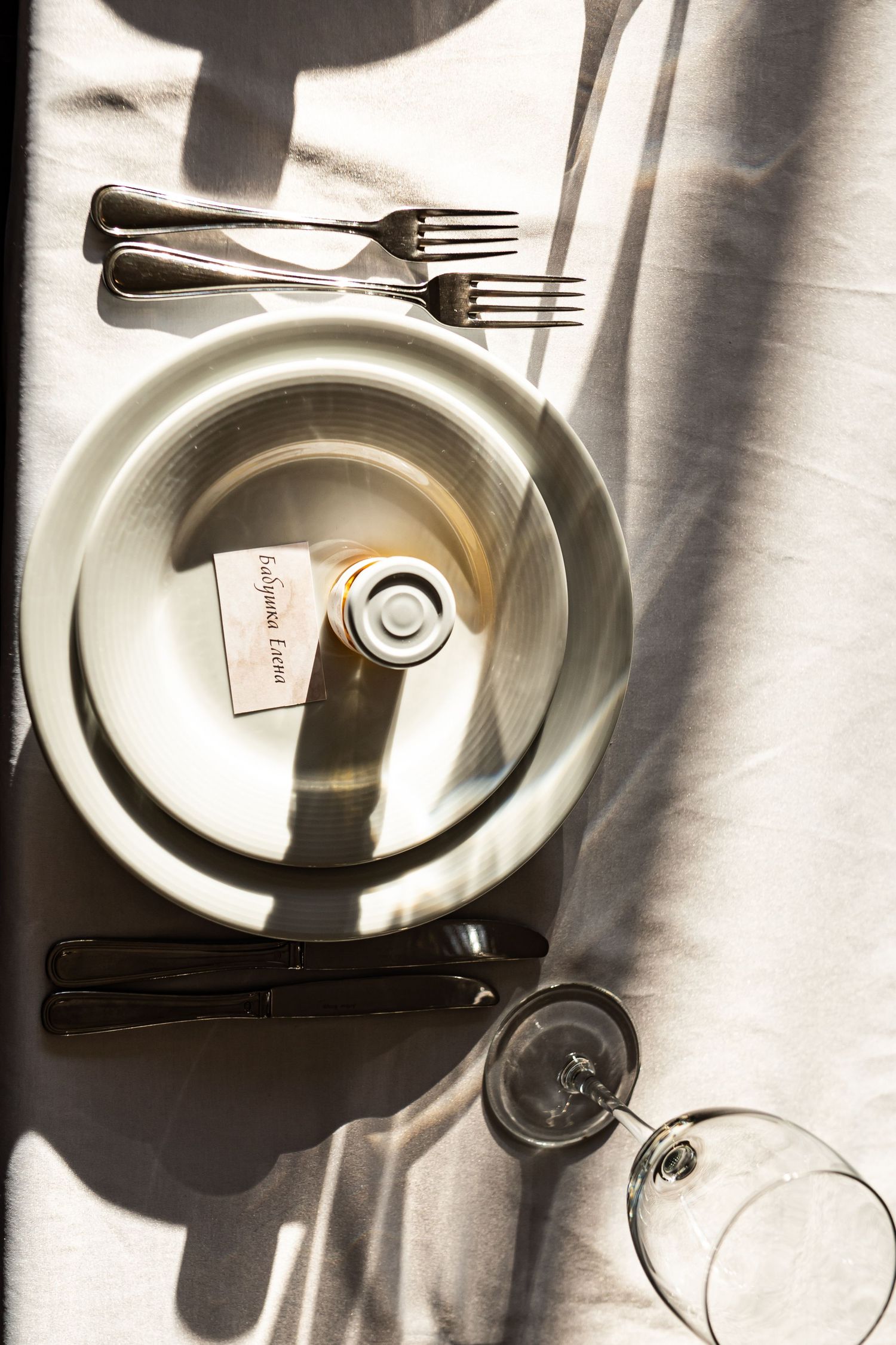 Overhead view of elegant table setting with white plate, silverware and wine glass casting dramatic shadows.