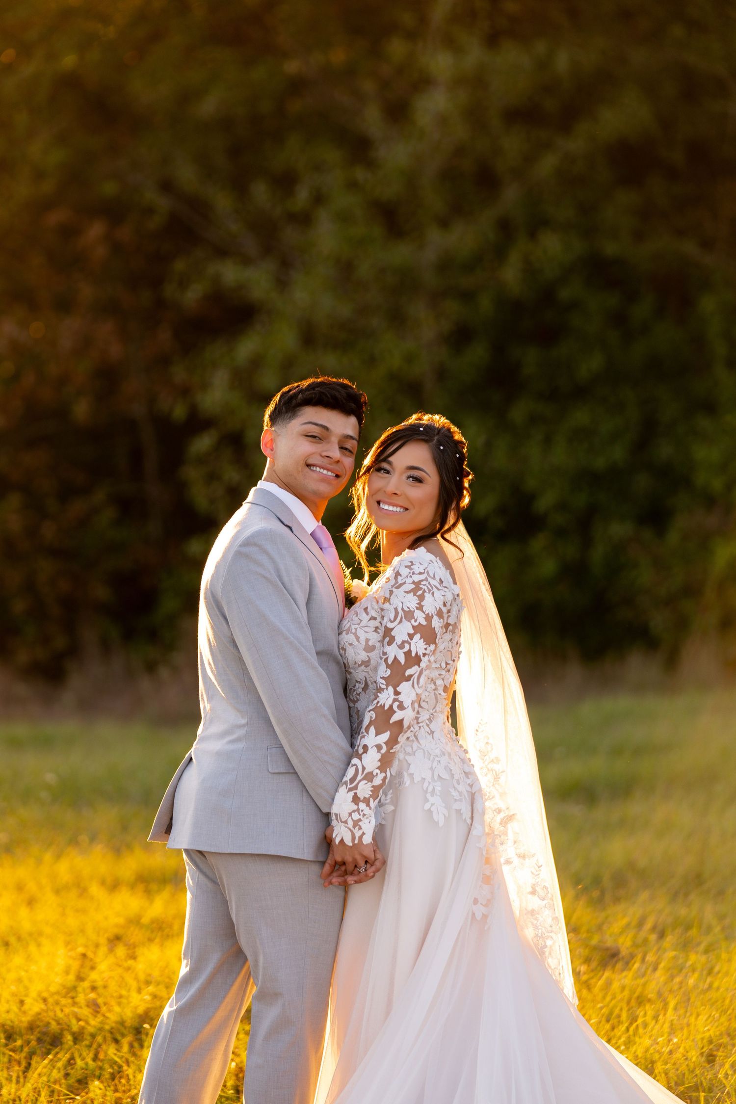 Wedding couple poses together in sunlit meadow during golden hour.