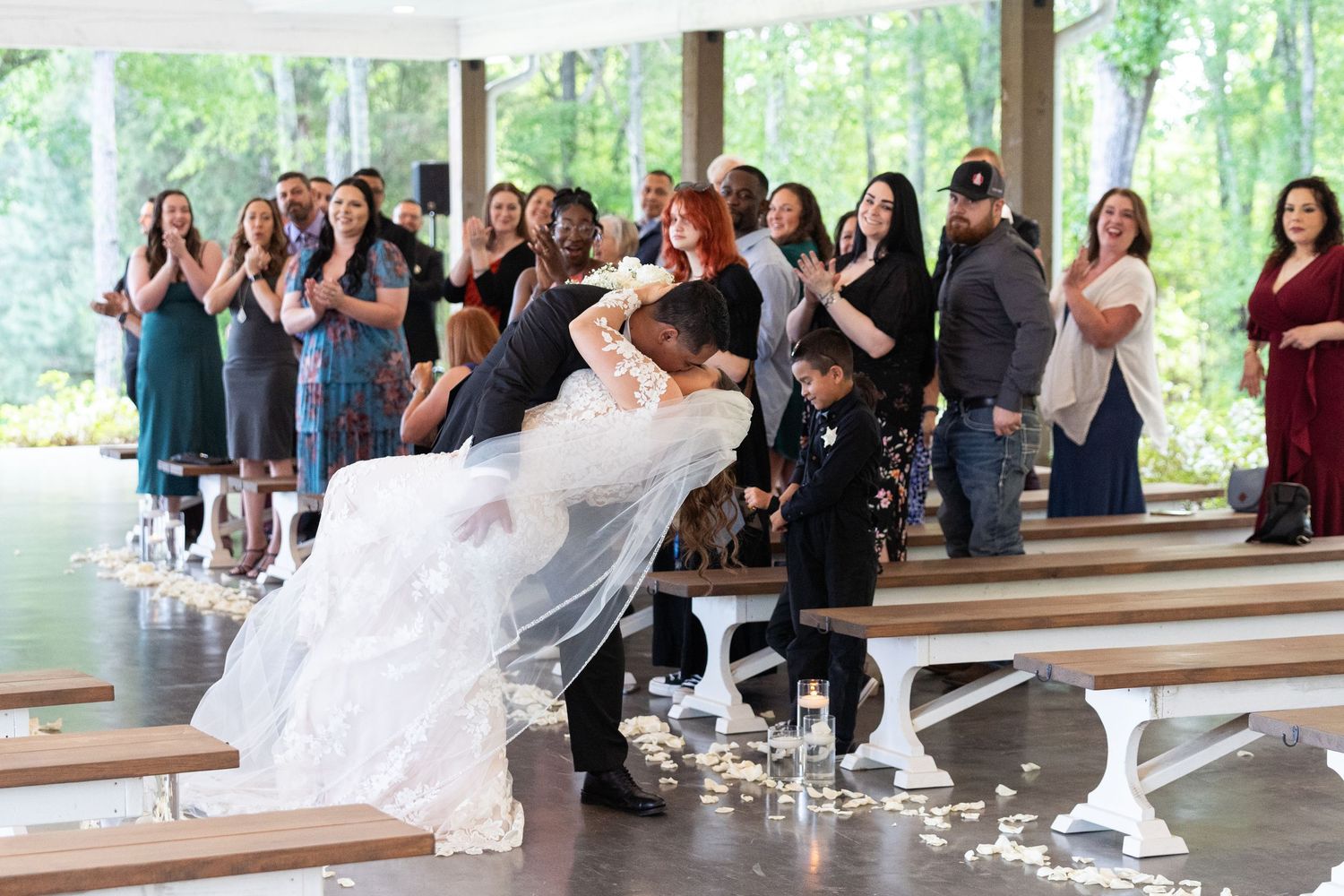 A couple performs a dramatic dance dip during their first dance at an outdoor covered wedding venue while guests watch.