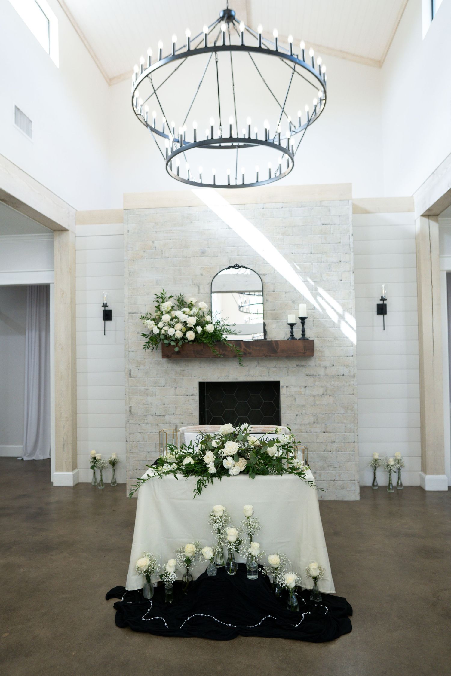 Modern white brick event venue with circular chandeliers and elegant floral arrangements on display tables.