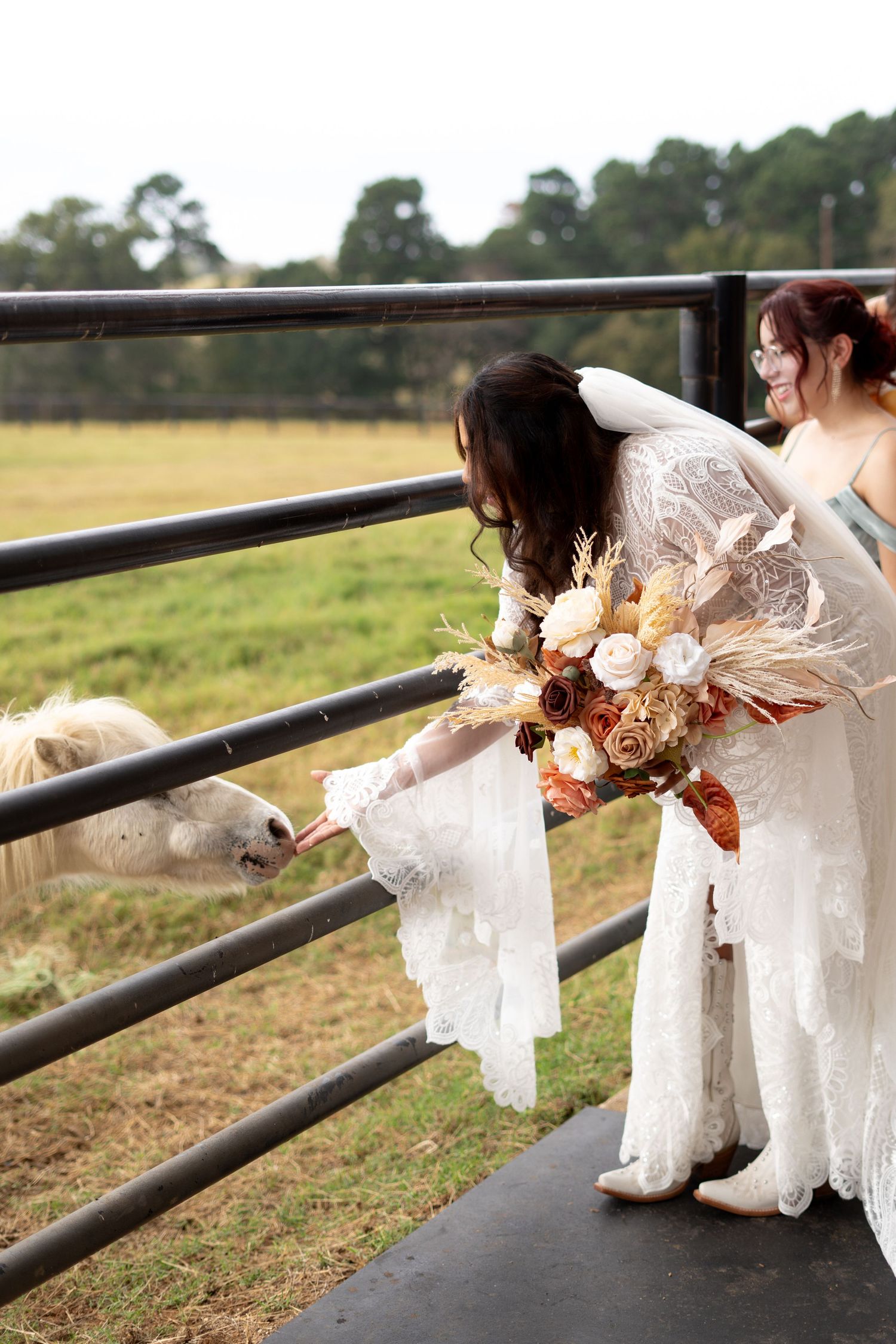 Wedding party sitting on rustic wooden fence with bouquets and white dresses.