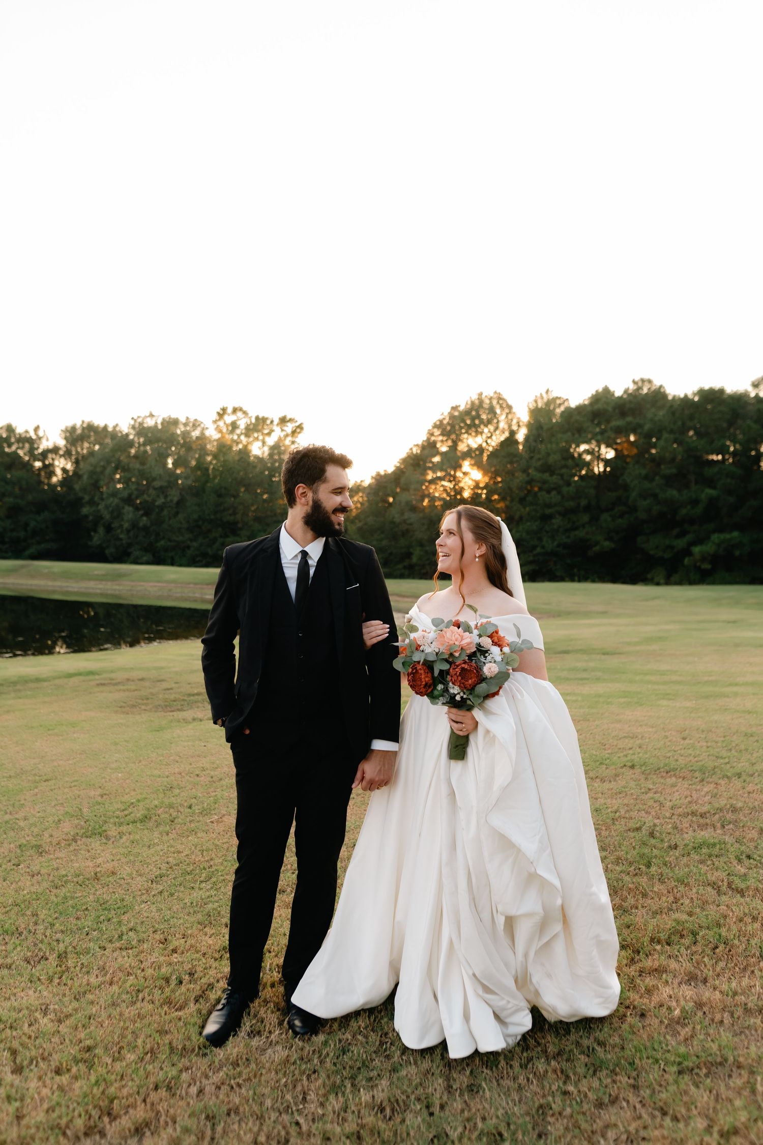 Wedding couple shares intimate moments in an open field during sunset with autumn colors in background.
