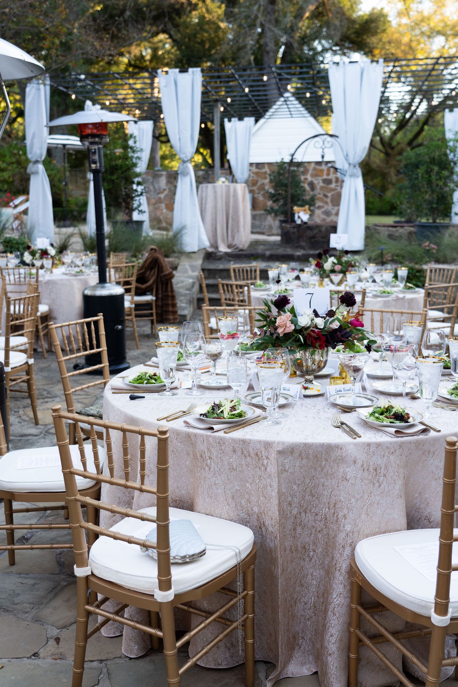 Elegant outdoor wedding reception setup with white linens and wooden chairs under draped canopy.