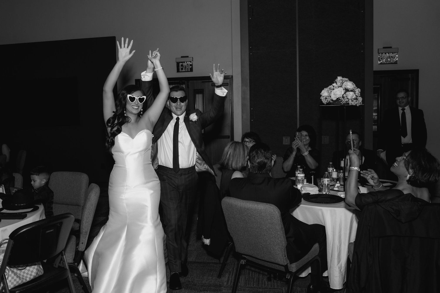 Black and white wedding reception photo showing dancing guests and a bride in a white dress on the dance floor.