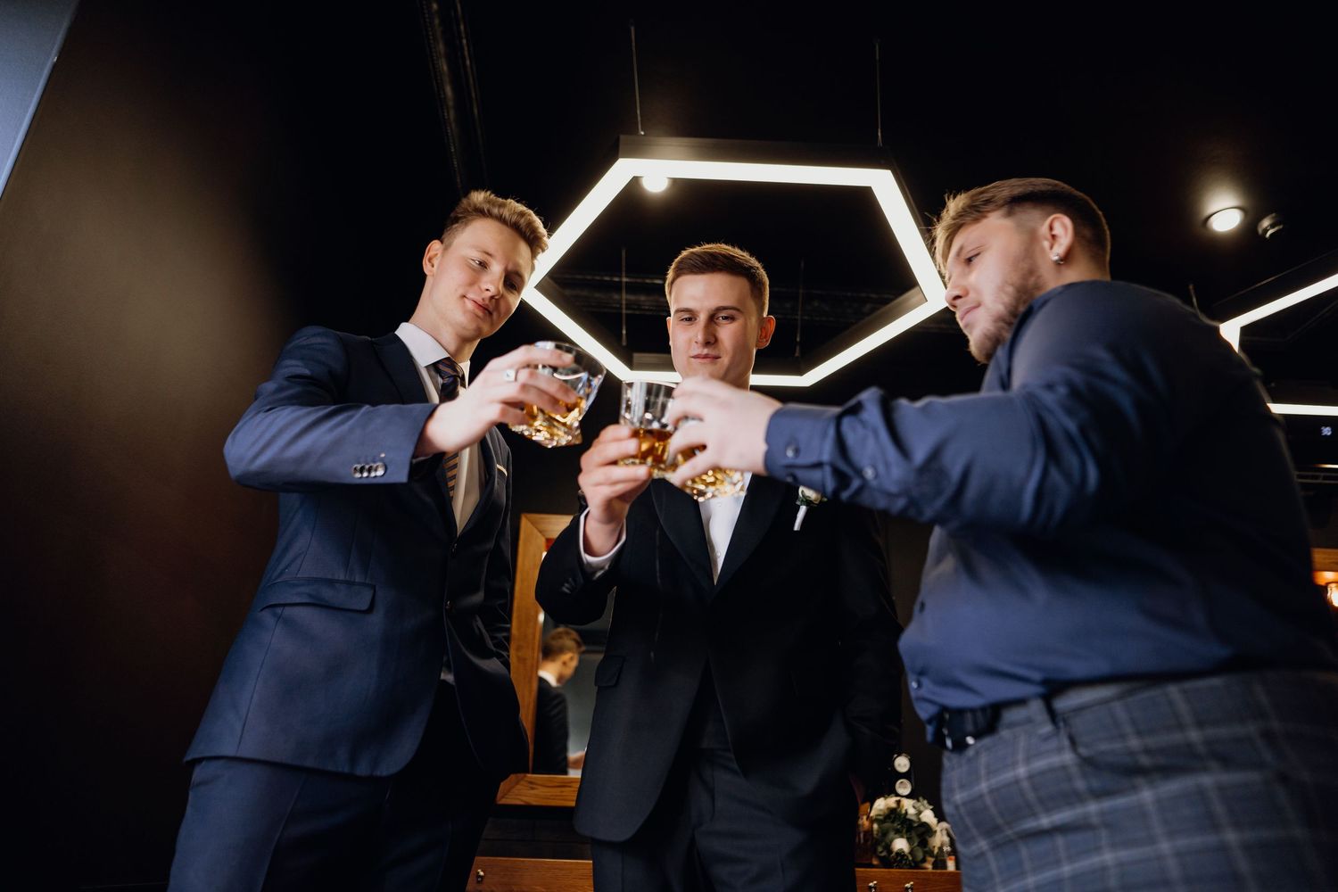 People in formal attire gather around illuminated hexagonal lighting fixtures in a dark room.