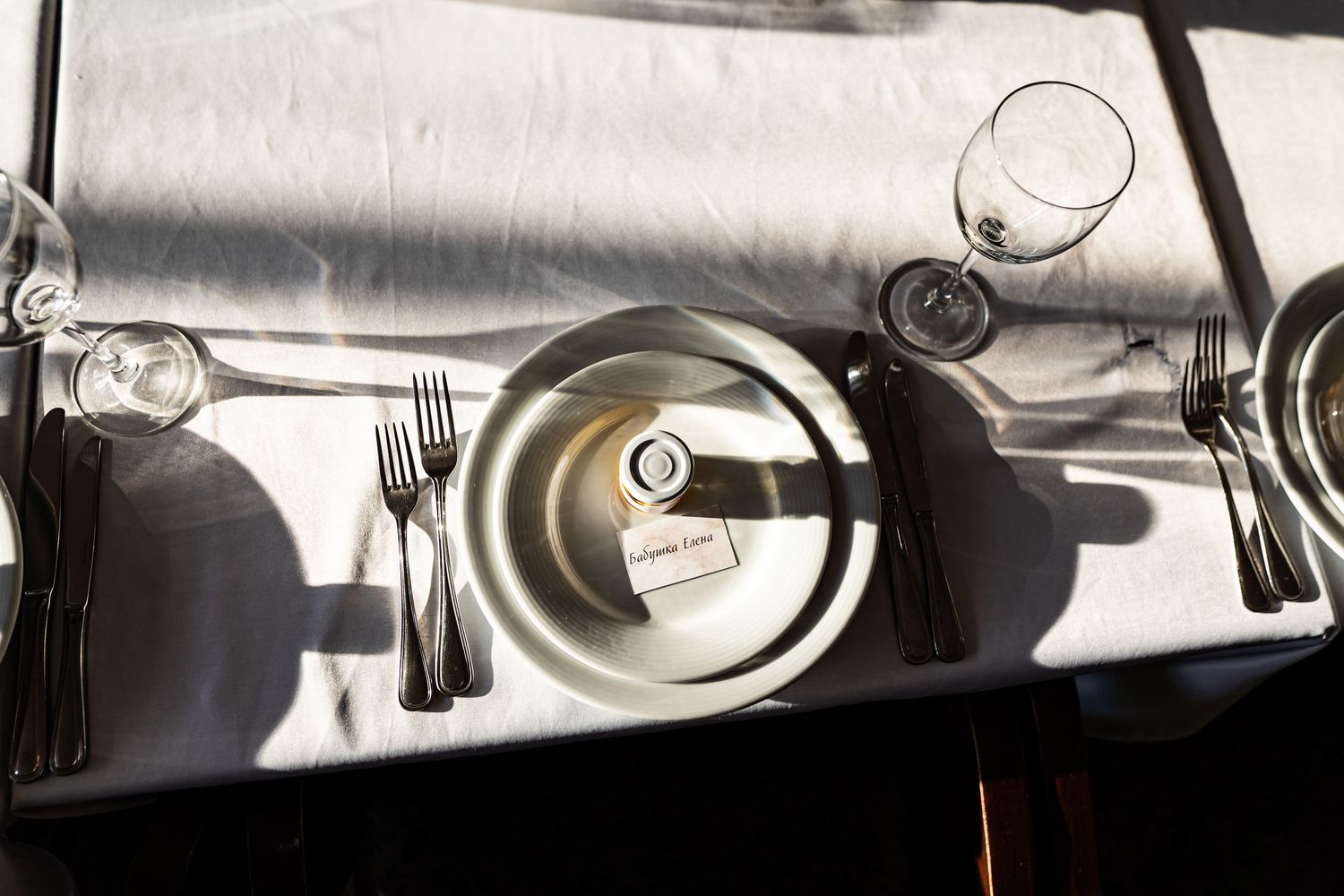 Overhead view of elegant place settings with plates, silverware and wine glasses casting dramatic shadows on white tablecloth.