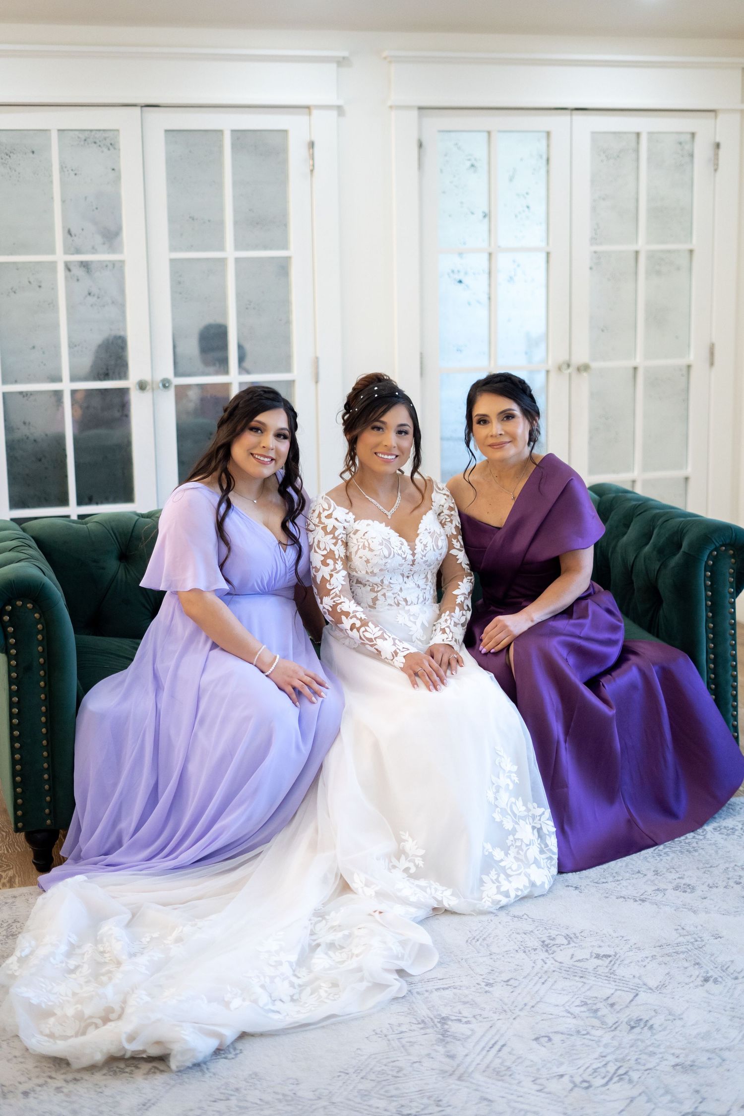 Bridal party lounging on emerald green couch in purple and white dresses.