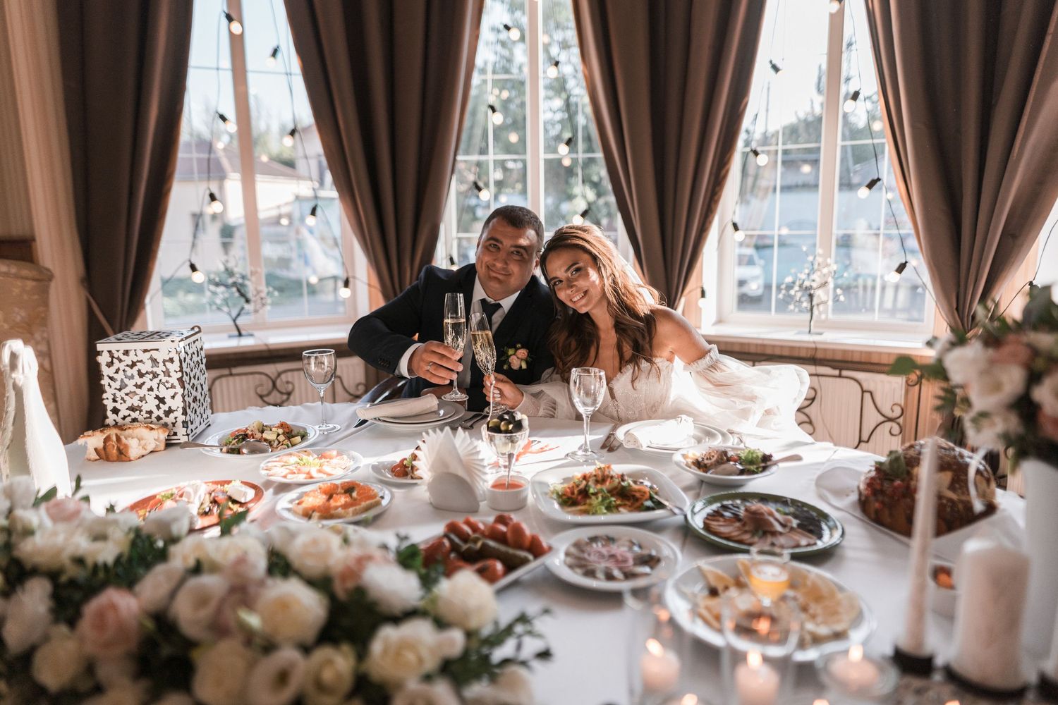 Elegant wedding reception tables adorned with white linens, floral centerpieces and decorative place settings in a bright room.