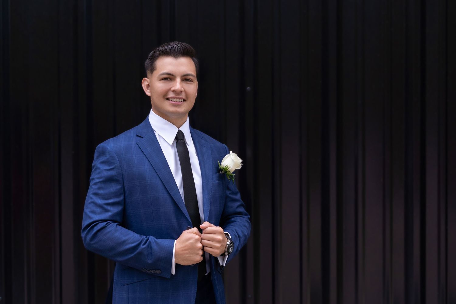 A person in a navy blue suit and tie stands on stage against a dark curtain background.