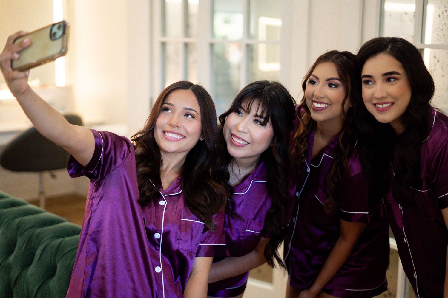 Wedding party wearing purple dresses taking selfies and laughing together.
