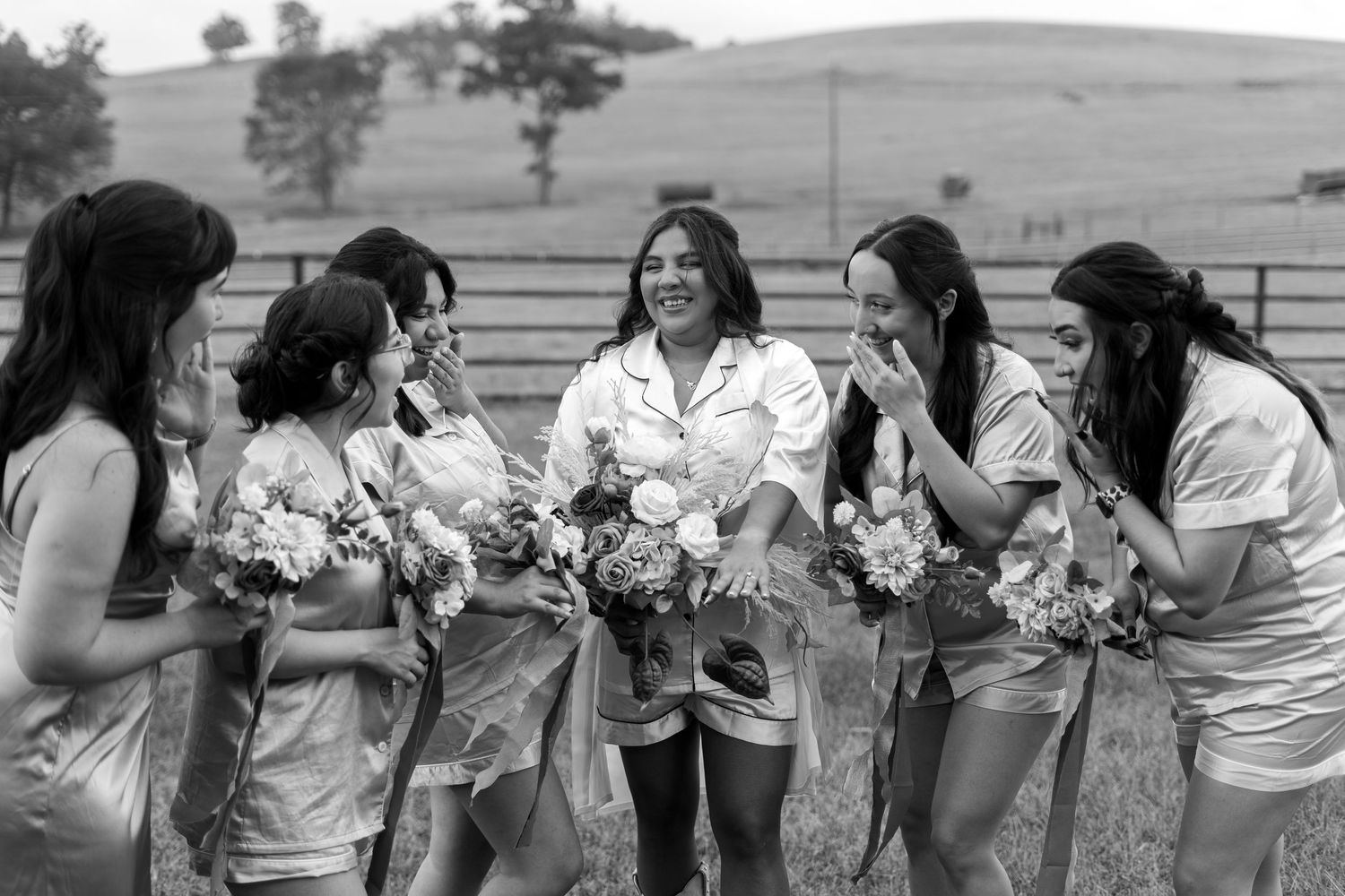 Bridesmaids in white dresses holding bouquets pose together outdoors.