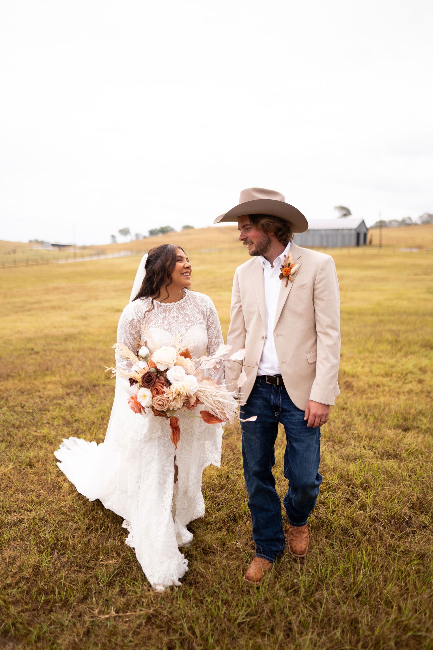 Bride and groom walking through a grassy field in rustic country wedding attire.