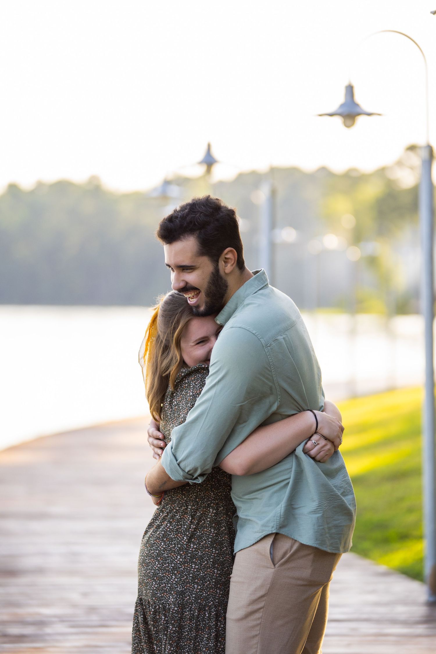 A joyful couple embraces on a waterfront boardwalk during golden hour.