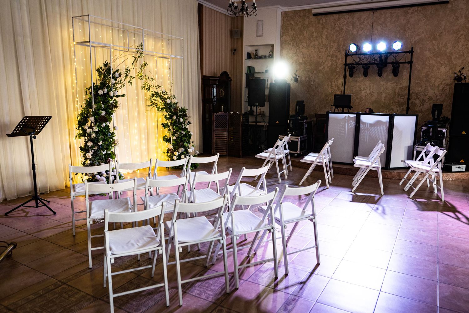 Indoor wedding ceremony setup with white chairs arranged in rows illuminated by soft purple lighting and decorative elements.